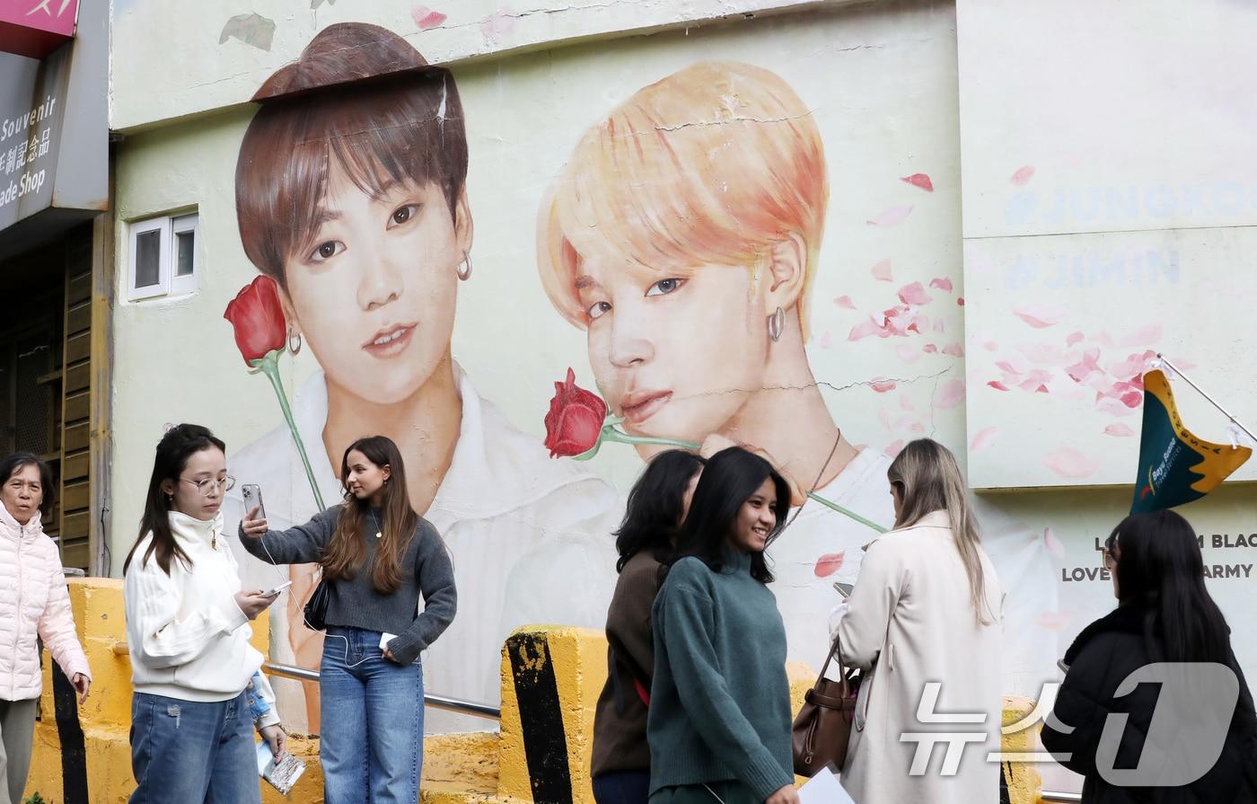 본문 이미지 - 방탄소년단(BTS) 컴백 공연을 이틀 앞둔 19일 부산 서구 감천문화마을에서 외국인 관광객들이 부산이 고향인 BTS 멤버 정국·지민이 그려진 대형 벽화를 배경으로 기념촬영을 하고 있다. 2026.3.19 ⓒ 뉴스1 윤일지 기자