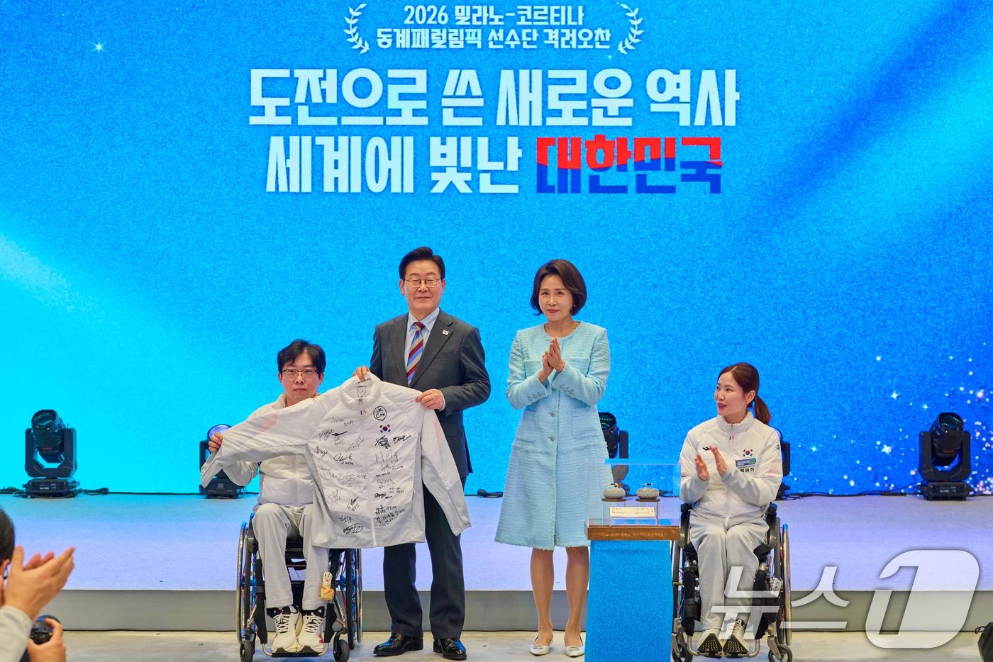 본문 이미지 - 이재명 대통령과 김혜경 여사가 지난 3월 청와대 영빈관에서 열린 밀라노-코르티나 동계 패럴림픽 선수단 격려 오찬에서 선수단 전원의 친필 사인이 담긴 단복과 컬링스톤 모형을 선물 받고 있다. (청와대 제공. 재판매 및 DB 금지) 2026.3.20 ⓒ 뉴스1 허경 기자
