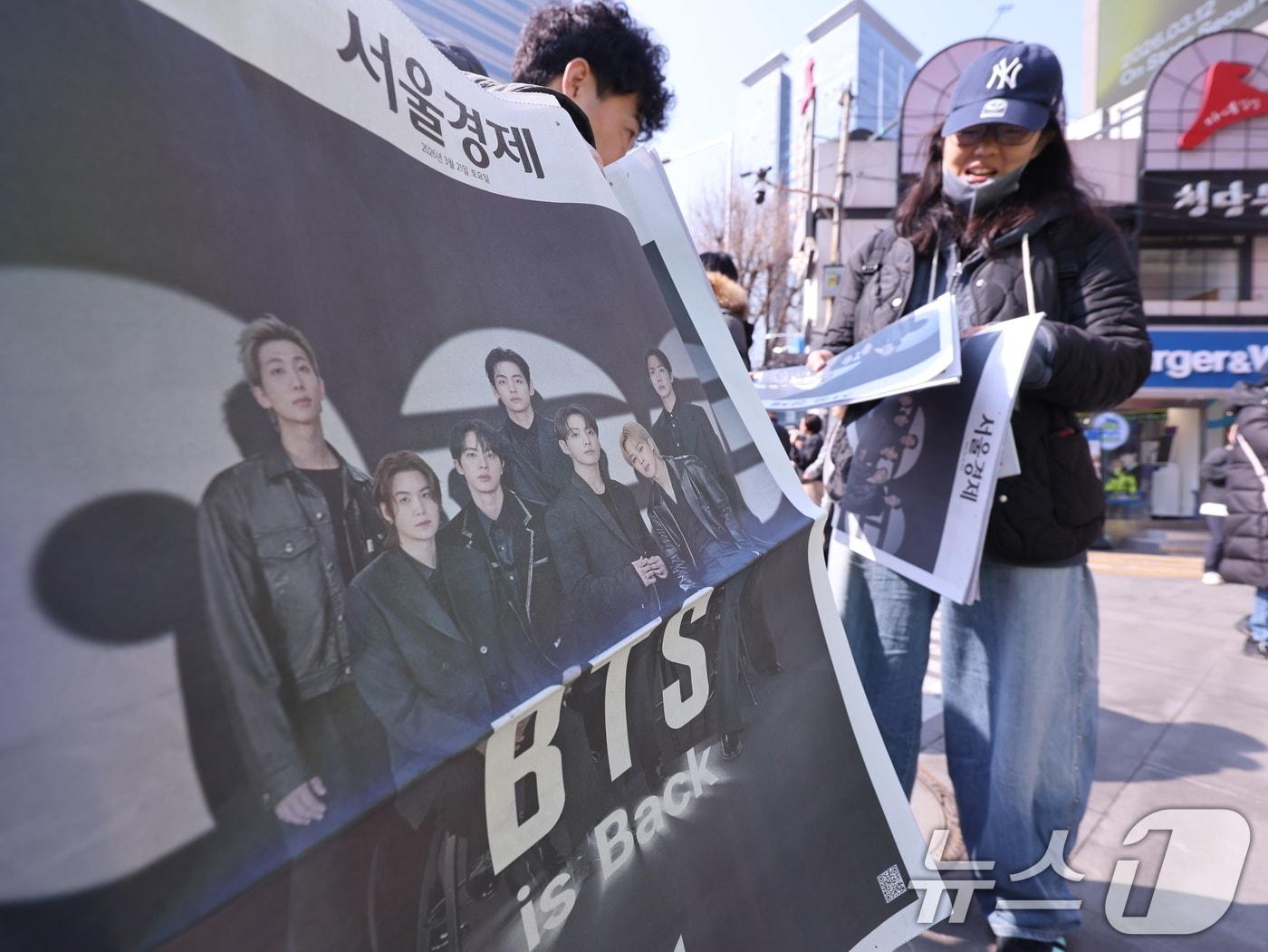 본문 이미지 - 방탄소년단(BTS) 컴백 공연일인 21일 오전 서울 광화문광장에서 외국인 관광객이 주요 일간지들이 발행한 BTS 관련 호외를 받고 있다. 2026.3.21 ⓒ 뉴스1 박지혜 기자