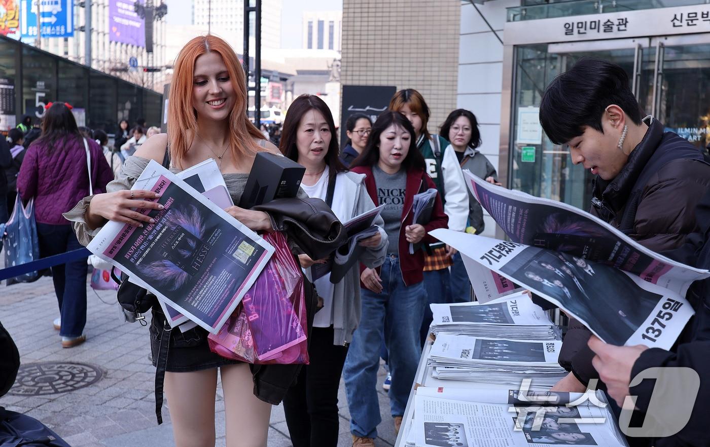 본문 이미지 - 방탄소년단(BTS) 컴백 공연일인 21일 오전 서울 광화문광장에서 외국인 관광객이 주요 일간지들이 발행한 BTS 관련 특별판을 받고 있다. 2026.3.21 ⓒ 뉴스1 박지혜 기자