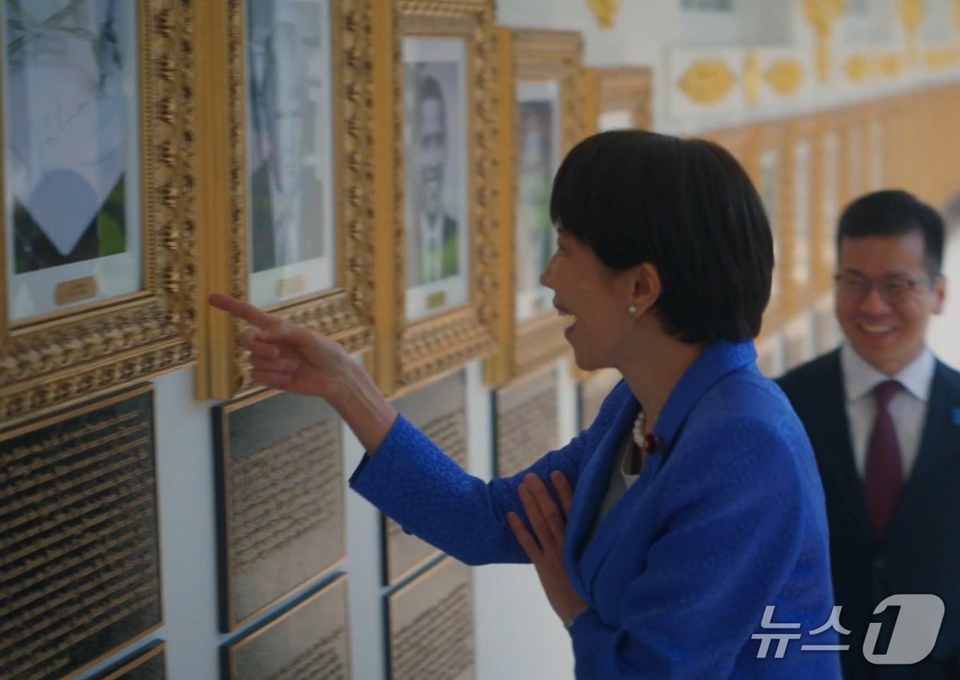 본문 이미지 - 다카이치 사나에 일본 총리가 조 바이든 전 대통령의 초상화 자리에 그의 서명을 기계가 대신 그려주는 '오토펜' 사진이 걸려있는 것을 보고  웃음을 터뜨리고 있다. (백악관 X)