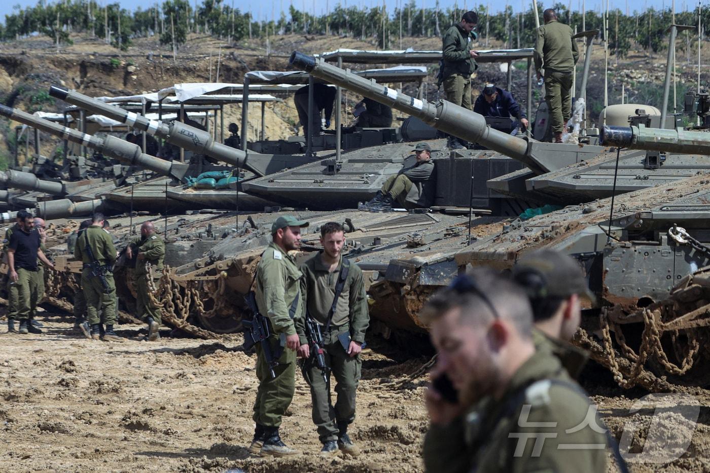 본문 이미지 - 23일(현지시간) 이스라엘 군인들이 이스라엘 북부의 레바논 국경 인근에 배치된 전차 옆에 서 있다. 2026.03.23. ⓒ 로이터=뉴스1