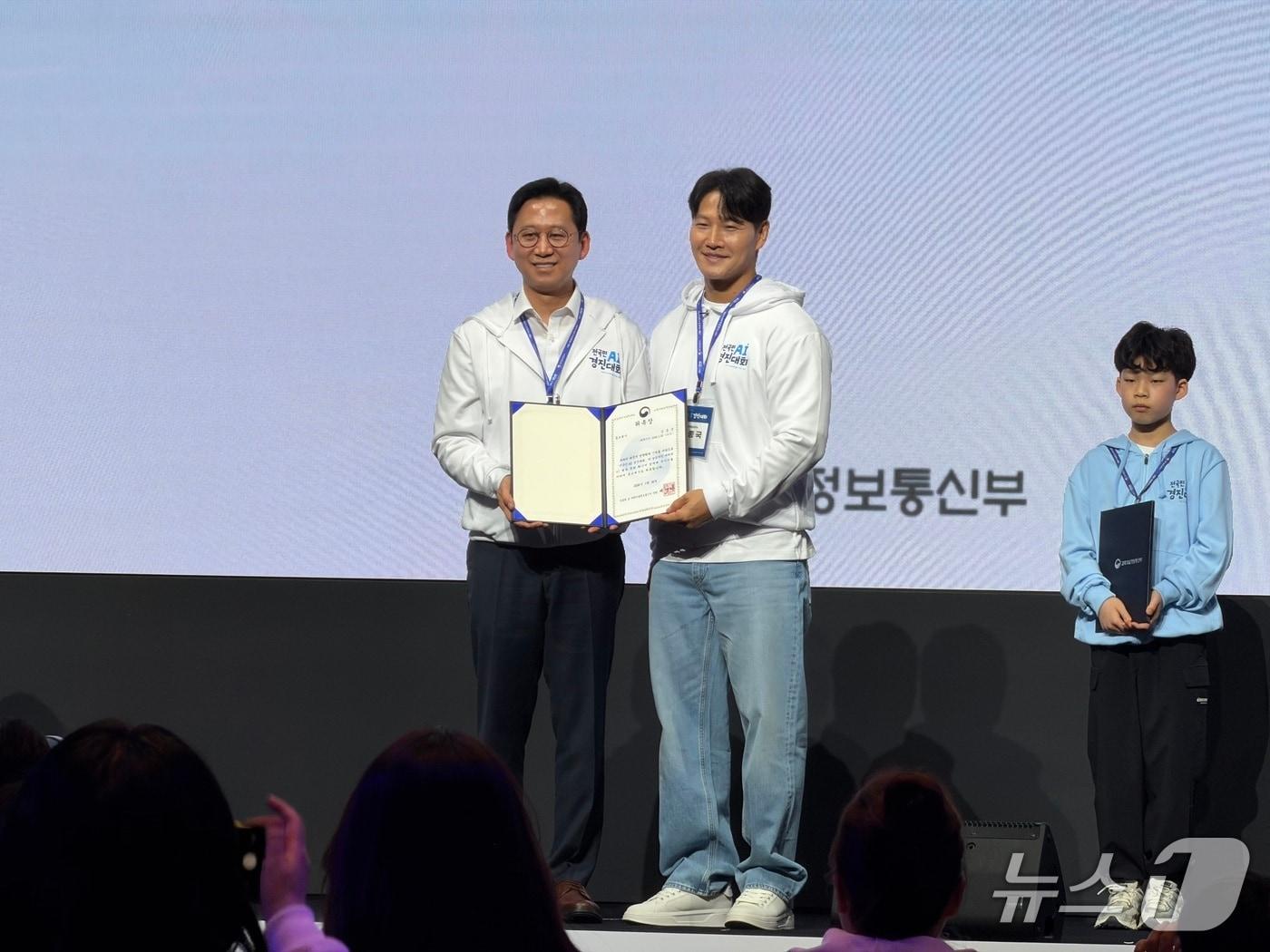 본문 이미지 - 26일 오후 서울 양재 엘타워에서 과학기술정보통신부 주최로 열린 '전 국민 AI 경진대회' 개막식에서 연예인 김종국이 홍보대사로 위촉됐다. (왼쪽부터) 배경훈 부총리 겸 과기정통부 장관, 연예인 김종국 2026.3.26 ⓒ 뉴스1 이기범 기자