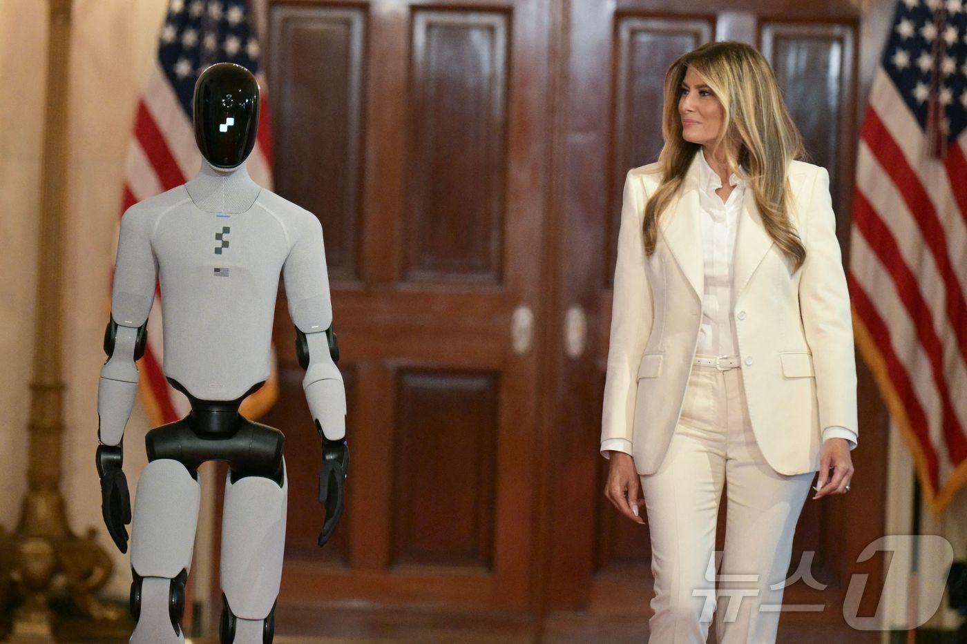본문 이미지 - 미국 영부인인 멜라니아 트럼프 여사가 25일(현지시간) 백악관에서 열린 한 행사에 휴머노이드 로봇과 함께 도착했다.2026.03.25. ⓒ AFP=뉴스1