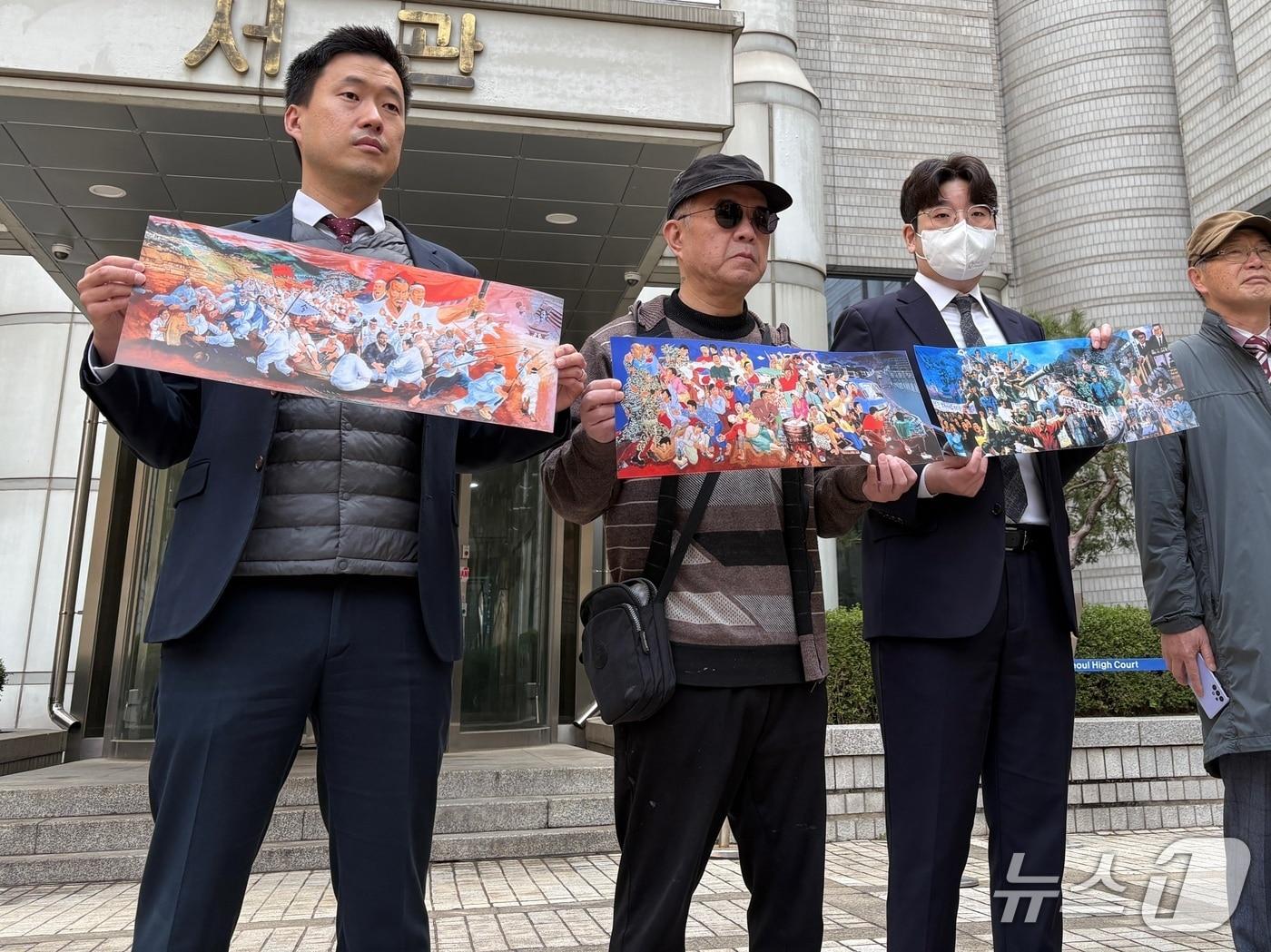 본문 이미지 - 애니메이션 감독 전승일 씨(가운데)와 변호인단이 27일 서울중앙지법 서관 앞에서 자신의 작품을 들고 있다. 2026.03.27 ⓒ 뉴스1 유수연 기자