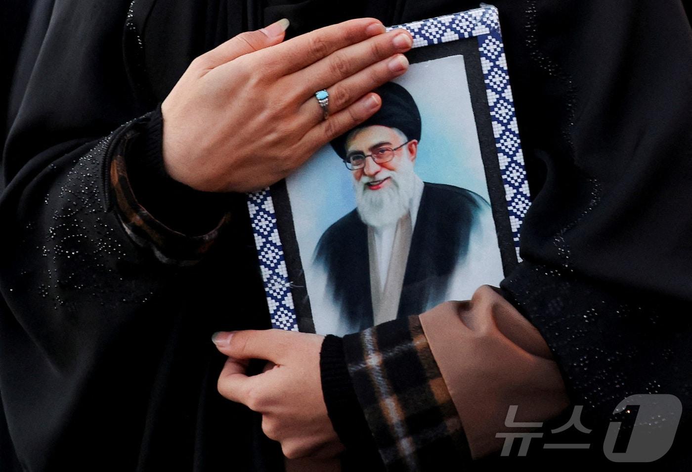 본문 이미지 - 사망한 하메네이 사진을 품에 안은 이란 테헤란의 한 주민. 2026.03.01 ⓒ 로이터=뉴스1