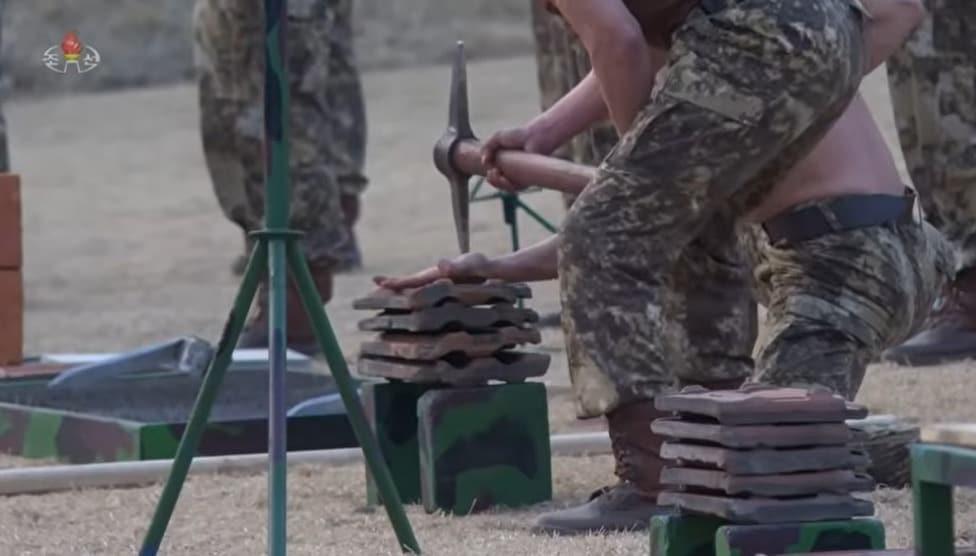 본문 이미지 - 조선중앙TV는 29일 전투원들이 김정은 노동당 총비서 앞에서 진행한 시범 장면을 보도했다. 기왓장 위에 있는 손을 낫으로 내려쳐 격차하는 모습. (조중TV 갈무리)