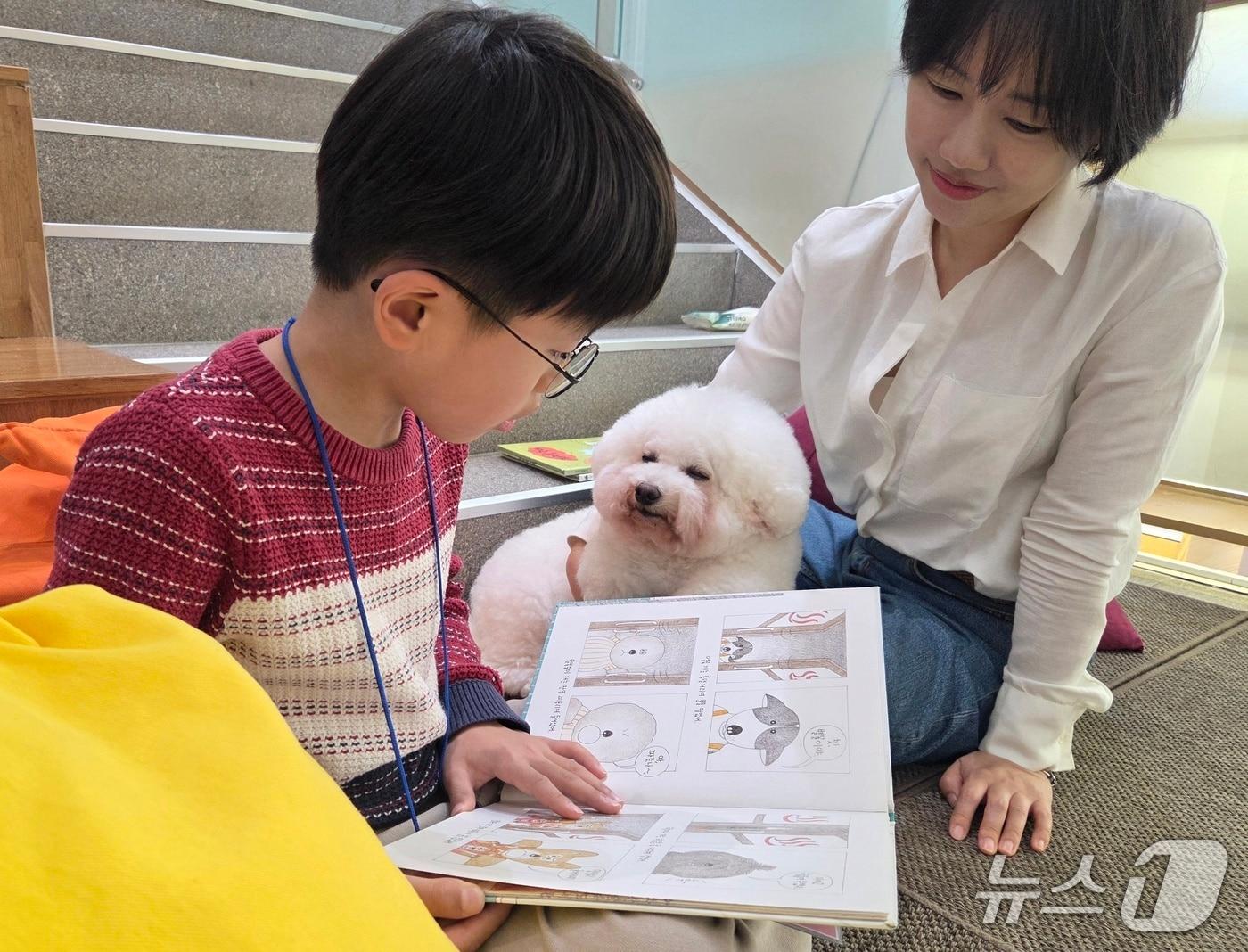 본문 이미지 - 한국인간동물상호작용연구회(카이)가 서울 광진구립아차산숲속도서관에서 진행한 동물매개 읽기 프로그램에서 김시현 어린이(왼쪽)가 리딩독 '홀릭이'에게 책을 읽어주고 있다. ⓒ 뉴스1 한송아 기자
