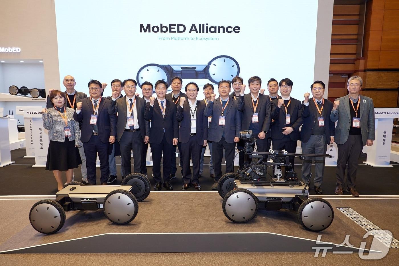 본문 이미지 - AW2026에서 열린 모베드 얼라이언스 출범식에서 기념사진을 촬영하는 모습. (왼쪽부터) 아르비젼 손영숙 대표, 현대트랜시스 김진우 상무, 위고로보틱스 박세일 대표, 성우하이텍 이동주 상무, 고성엔지니어링 최창신 대표, 모베이스 송기갑 상무, LS티라유텍 김정하 대표, 서연이화 강상욱 상무, 현대차·기아 로보틱스랩 현동진 상무, SL 정문호 대표, 한국AI·로봇산업협회 김재환 상임이사, PHA 홍성율 전무, 가온로보틱스 이진성 대표, 성주음향 최선용 대표, 주식회사 로아스 주용 대표, 현대성우 윤형석 대표, BH-EVS 김진용 대표. (현대차그룹 제공)