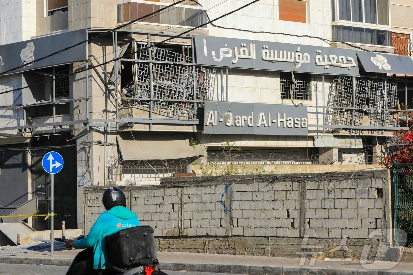 본문 이미지 - 2024년 10월 21일, 이스라엘의 야간 공습으로 베이루트 남부 교외에 위치한 알카르드 알하산 금융그룹 지점이 공격을 받은 현장을 한 남성이 오토바이를 타고 지나가고 있다.2024.10.21. ⓒ AFP=뉴스1