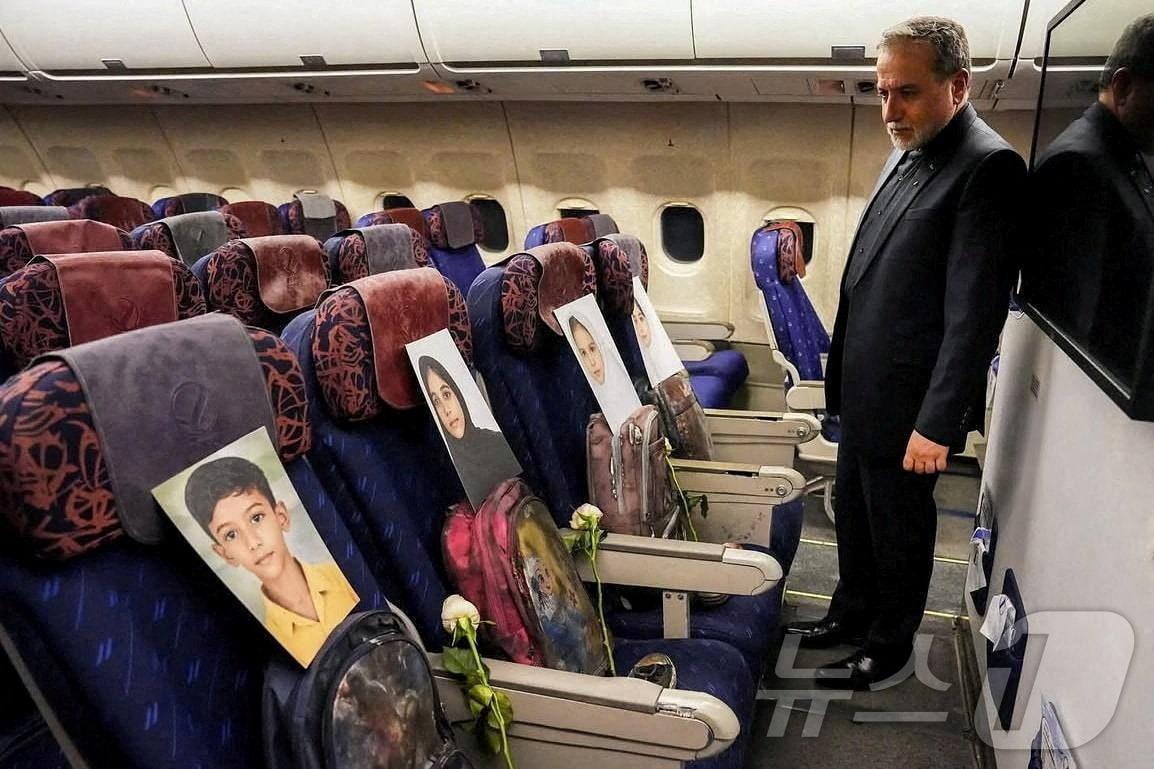 본문 이미지 - 아바스 아라그치 이란 외무장관의 미국과의 협상장으로 향하는 기내로 추정되는 장소에서 미국-이스라엘 공습으로 희생된 어린이들의 영정 사진과 유품을 바라보고 있다. 2026.04.11 ⓒ 로이터=뉴스1