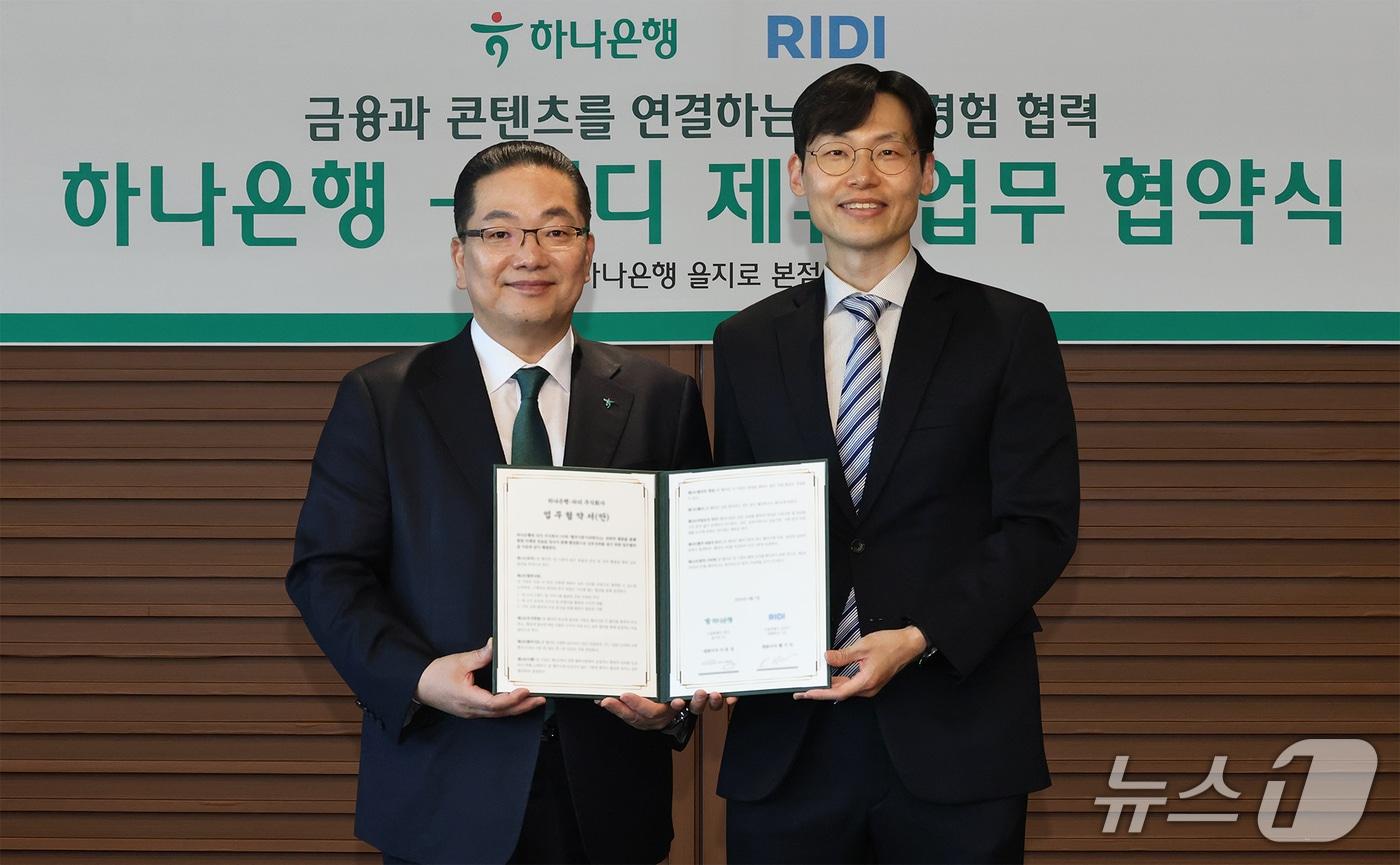 본문 이미지 - 이호성 하나은행장(왼쪽)과 배기식 리디 대표이사가 협약서를 들고 기념촬영을 하고 있다(하나은행 제공).