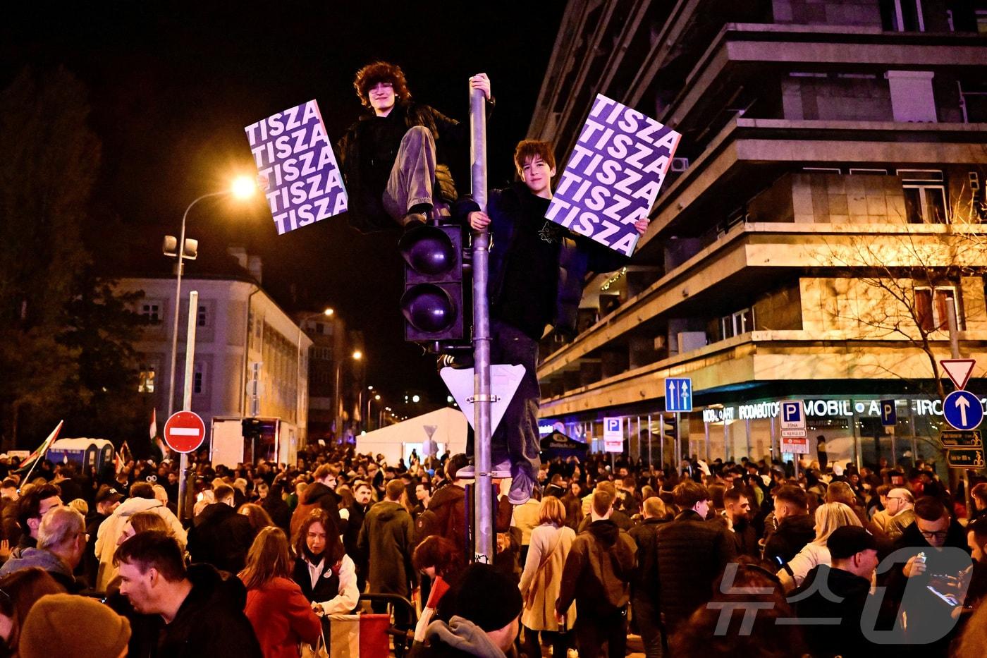 본문 이미지 - 12일(현지시간) 헝가리 총선 부분 개표 결과 발표 이후 부다페스트에서 일부 사람들이 야당인 티서당 이름이 적힌 펫말을 들고 있다. 2026.4.13. ⓒ 뉴스1 ⓒ 로이터=뉴스1