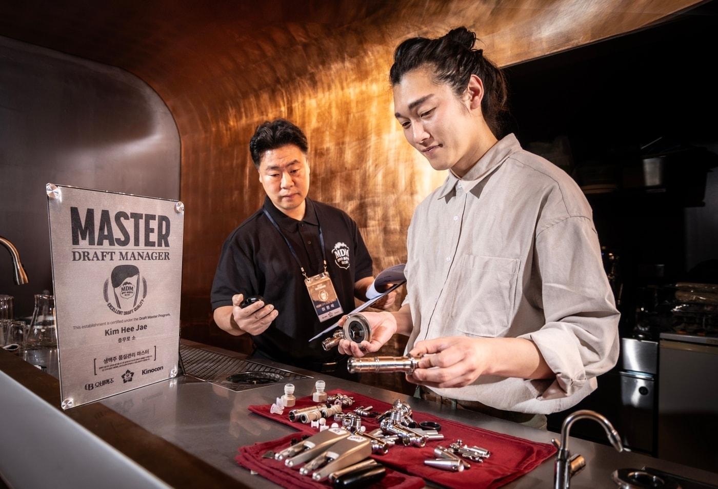 본문 이미지 -  오비맥주와 함께 MDM 자격 제도를 운영하는 키노콘 감독관이 MDM 1호점인 서울 충무로 선술집 '소'를 방문해 (오른쪽)김희재 대표가 생맥주 위생관리 절차에 맞게 생맥주 공급 라인을 관리하는지 중간 점검하고 있다.(오비맥주 제공)