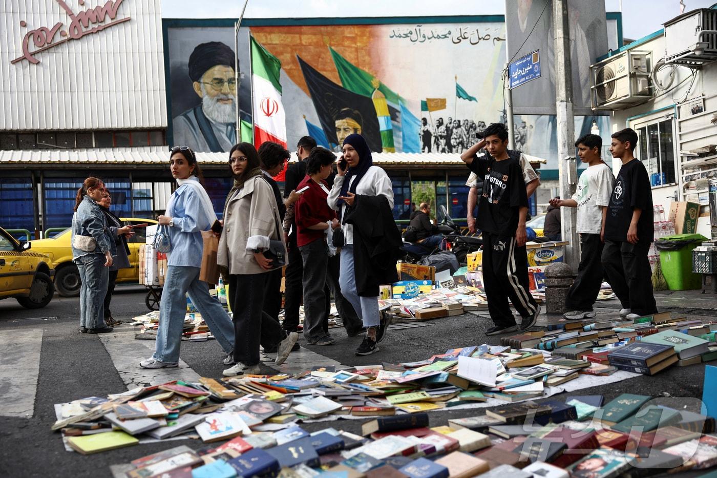 본문 이미지 - 13일(현지시간) 이란 테헤란에서 시민들이 이란의 전 최고 지도자 아야톨라 알리 하메네이의 벽화 옆을 지나가고 있다. 2026.04.13 ⓒ 로이터=뉴스1