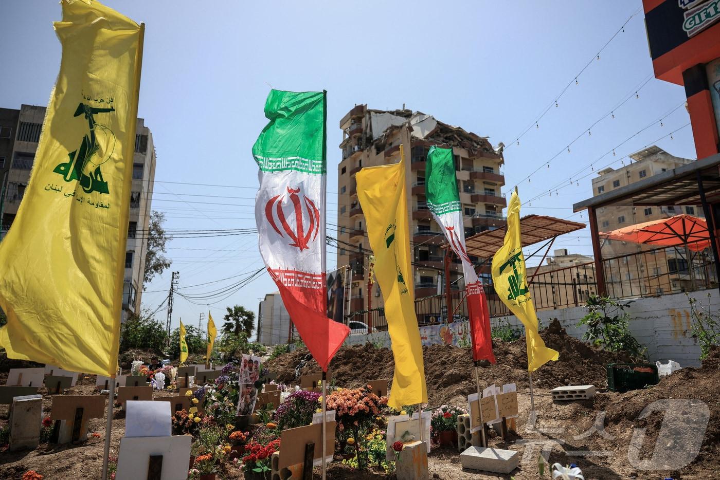 본문 이미지 - 레바논 남부 티레에서 16일(현지시간) 손상된 건물 옆 임시 묘지에서 헤즈볼라와 이란 국기가 펄럭이고 있다. 2026.4.16 ⓒ 로이터=뉴스1