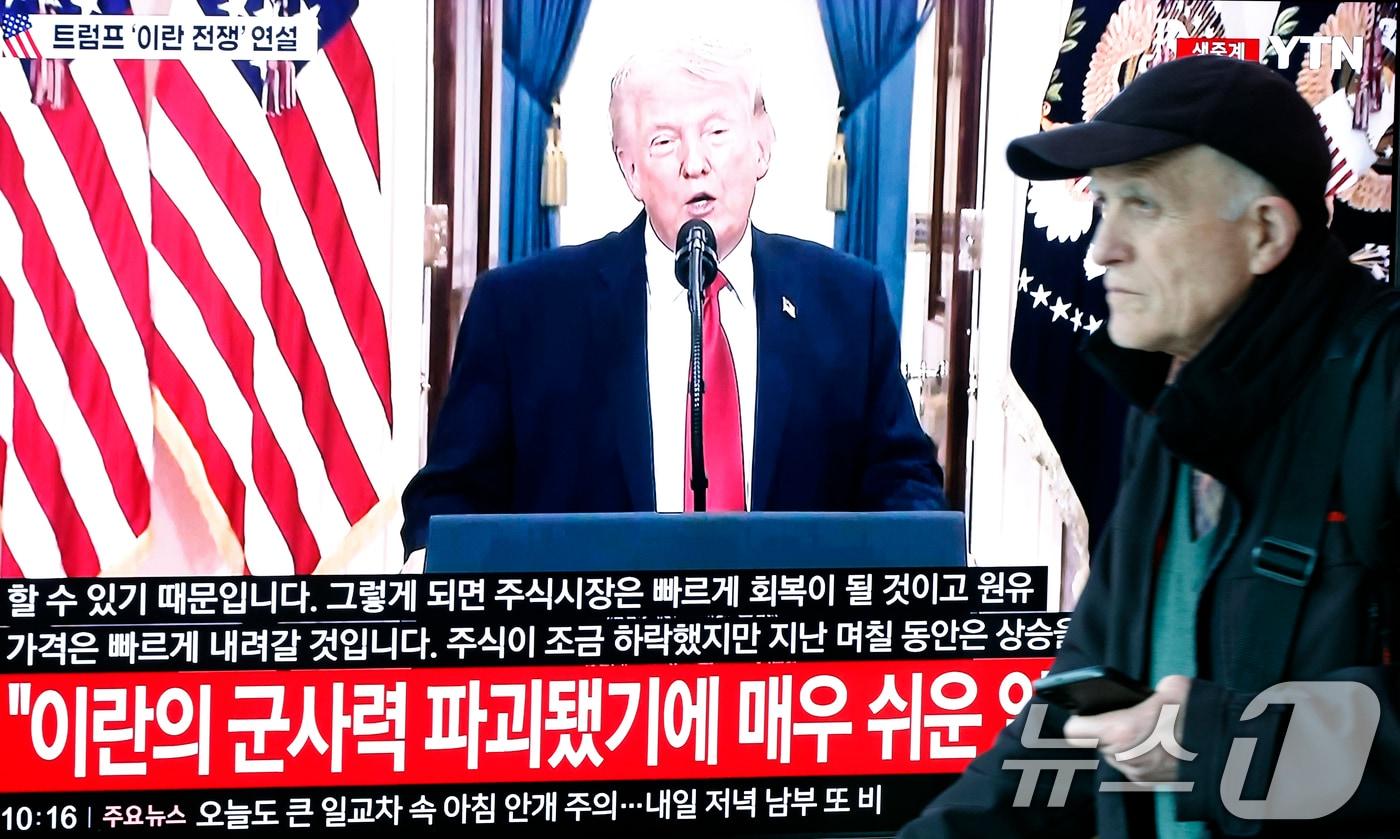 본문 이미지 - 2일 오전 서울시 용산구 서울역 대합실에서 한 외국인 관광객이 도널드 트럼프 미국 대통령의 이란 전쟁 상황 관련 대국민 연설 TV 생중계 앞을 지나고 있다. 2026.4.2 ⓒ 뉴스1 박정호 기자