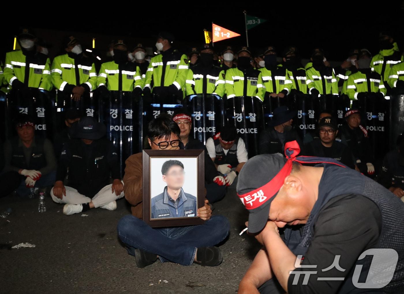 본문 이미지 - 20일 경남 진주시 정촌면 CU 진주물류센터 앞에서 화물연대 노조원이 집회 중 2.5톤 화물차에 치어 숨진 노조원의 영정을 들고 슬픔에 잠겨 있다. 이날 현장에서는 화물차와 집회 참가자 3명이 충돌해 1명이 숨지고 2명이 다치는 사고가 발생했다. 2026.4.20 ⓒ 뉴스1 윤일지 기자