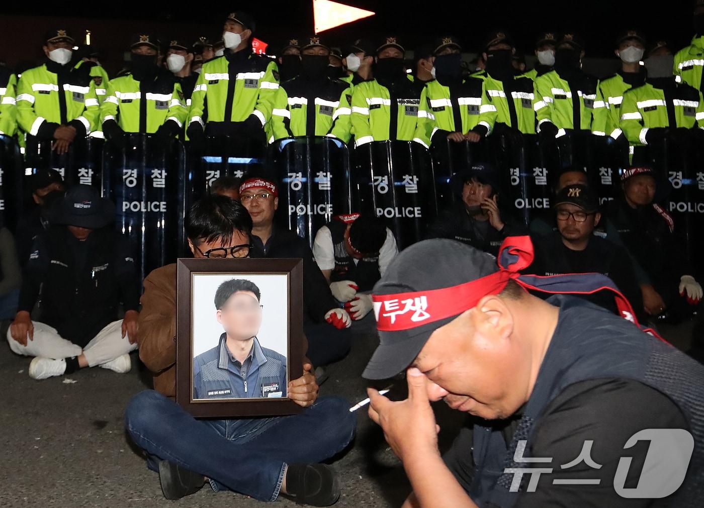 본문 이미지 - 20일 경남 진주시 정촌면 CU 진주물류센터 앞에서 화물연대 노조원이 집회 중 2.5톤 화물차에 치어 숨진 노조원의 영정을 들고 슬픔에 잠겨 있다. 이날 현장에서는 화물차와 집회 참가자 3명이 충돌해 1명이 숨지고 2명이 다치는 사고가 발생했다. 2026.4.20 ⓒ 뉴스1 윤일지 기자