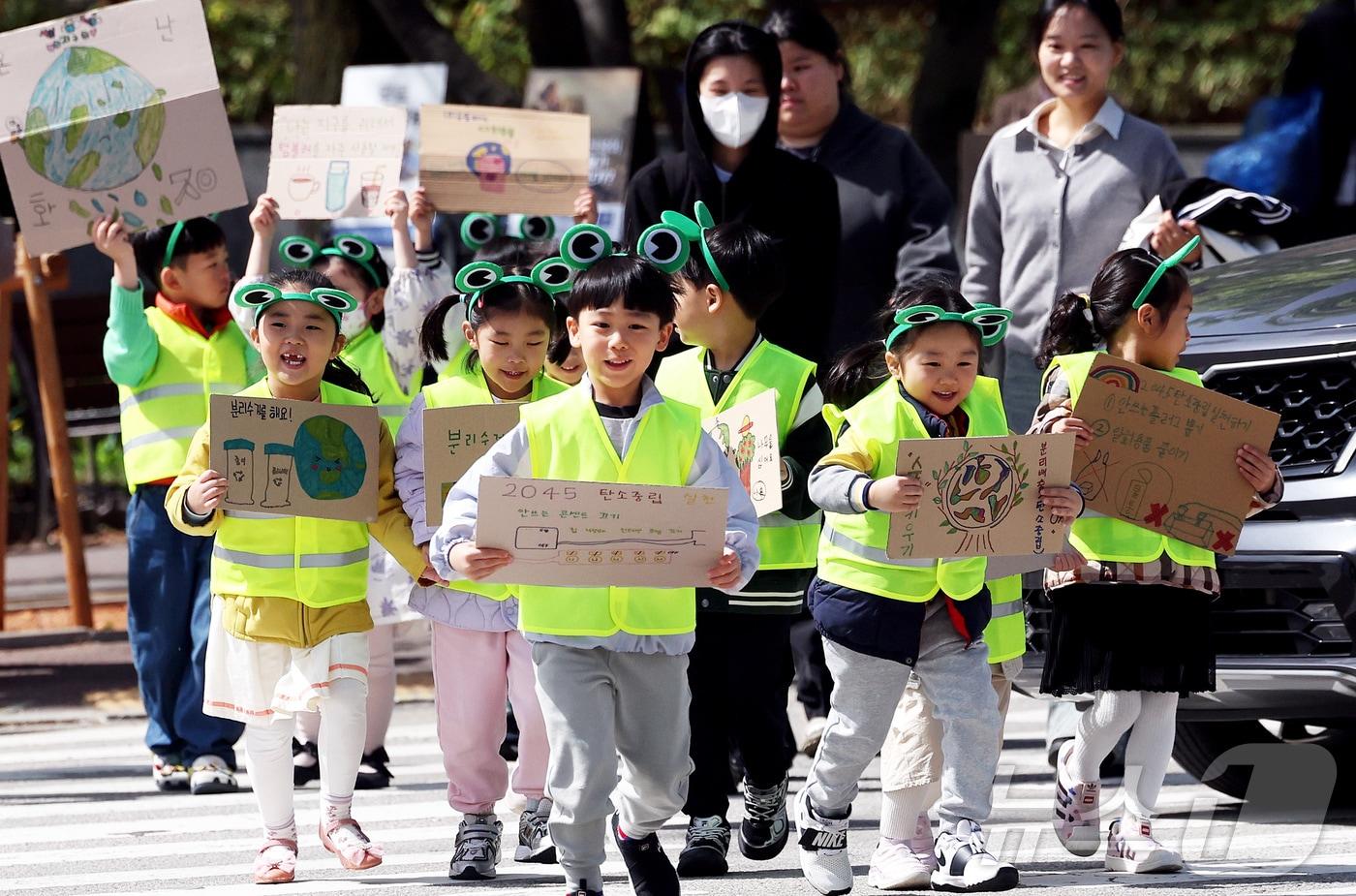 본문 이미지 - 지구의 날을 앞두고 광주 북구청직장어린이집 아이들과 구청 기후환경과 직원들이 북구청 교차로에서 일회용품 사용 자제와 탄소중립 손팻말을 들고 지구 살리기 길거리 퍼포먼스를 펼치고 있다. (광주 북구 제공. 재판매 및 DB 금지) 2026.4.21 ⓒ 뉴스1 박지현 기자