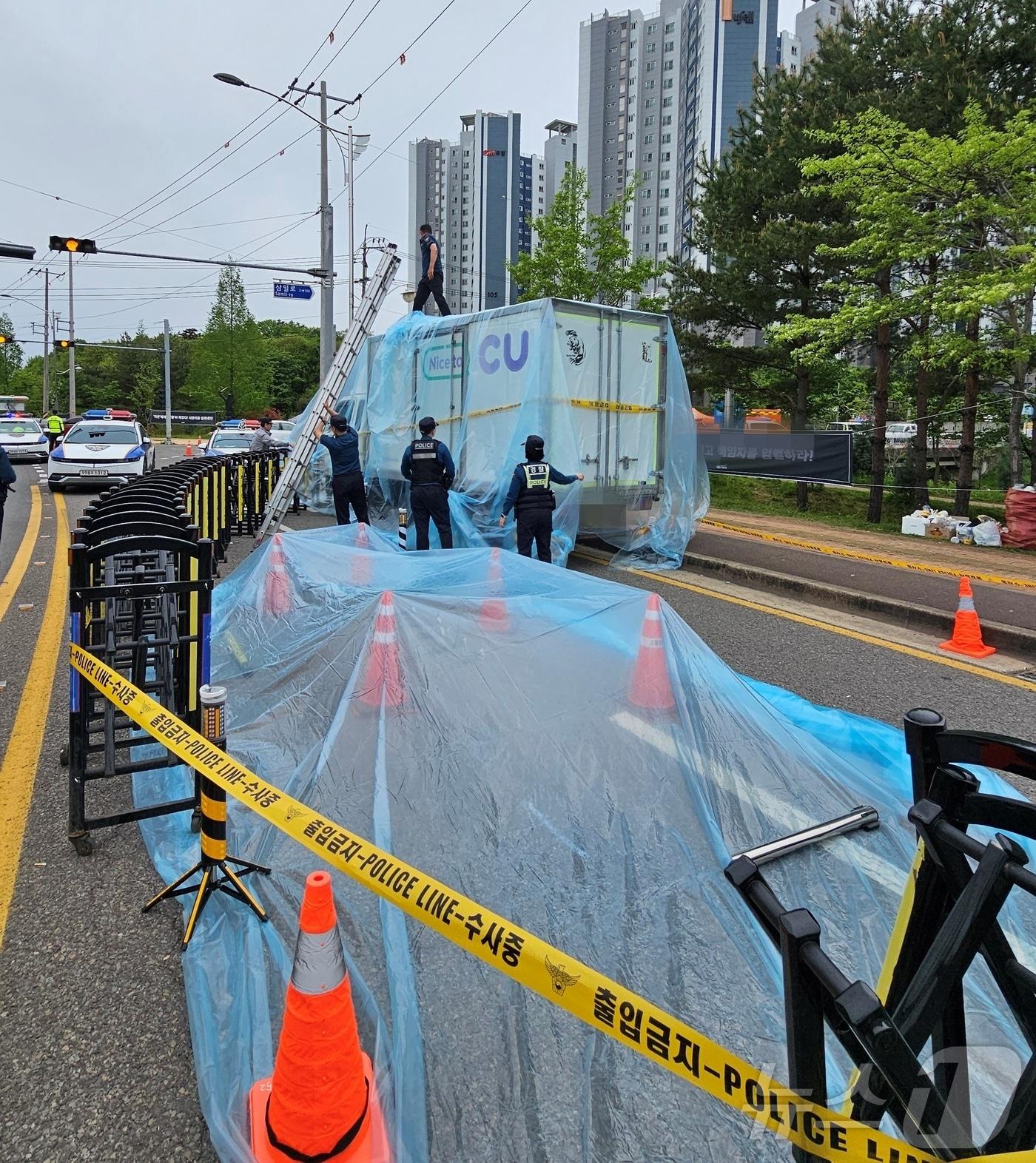 본문 이미지 - 22일 경남 진주시 정촌면 CU 진주물류센터 앞에서 경찰이 민주노총 화물연대 조합원이 사망한 사고 현장 보존을 위해 방수포 작업을 하고 있다. 2026.4.22 ⓒ 뉴스1 한송학 기자