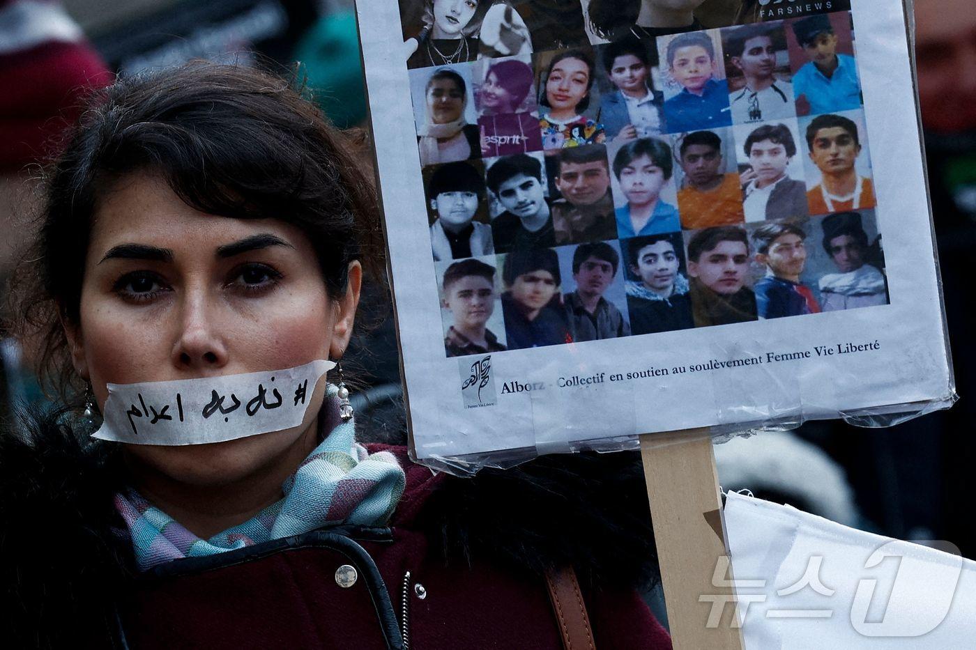 본문 이미지 - 2026년 1월 31일 프랑스 파리에서 열린 침묵 행진에서 한 시위자가 입에 “사형 반대(no execution)”라는 문구가 적힌 스티커를 붙이고, 이란 정부의 반정부 시위 탄압으로 희생된 것으로 알려진 피해자들의 초상화 옆에 서 있다. 2026.01.31. ⓒ AFP=뉴스1