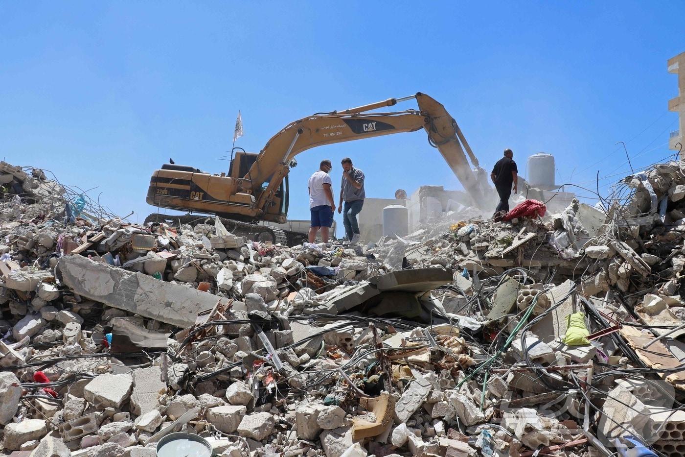 본문 이미지 - 23일(현지시간) 레바논 남부 티르의 한 주거 지역에서 주민 모하마드 알리 히자지(왼쪽)가 무너진 건물 잔해를 치우는 굴착기 옆에 서 있다. 그는 이스라엘의 공습으로 목숨을 잃은 가족들의 유품을 찾기 위해 잔해 더미를 뒤지고 있었다. 2026.04.23. ⓒ AFP=뉴스1