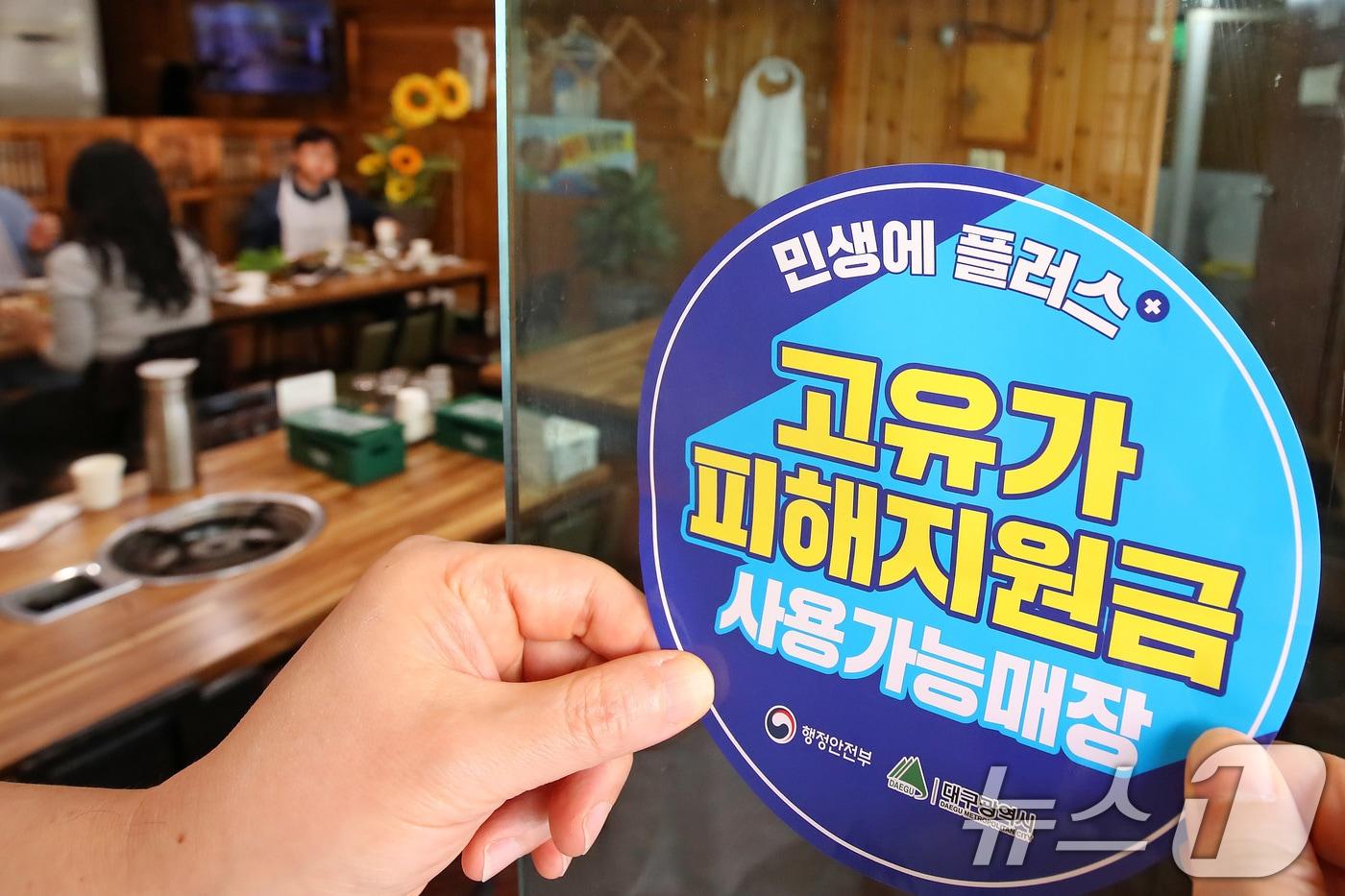 본문 이미지 - 고유가 피해지원금 1차 지급이 시작된 27일 대구 수성구 한 음식점에서 상인이 고유가 피해지원금 사용 가능 매장을 알리는 스티커를 붙이고 있다. 2026.4.27 ⓒ 뉴스1 공정식 기자