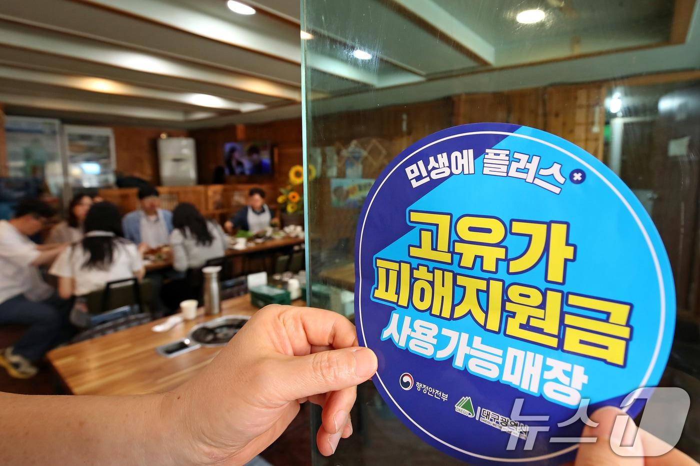 본문 이미지 - 고유가 피해지원금 1차 지급이 시작된 지난 4월 27일 대구 수성구의 한 음식점에서 상인이 고유가 피해지원금 사용 가능 매장을 알리는 스티커를 붙이고 있다. 2026.4.27 ⓒ 뉴스1 공정식 기자