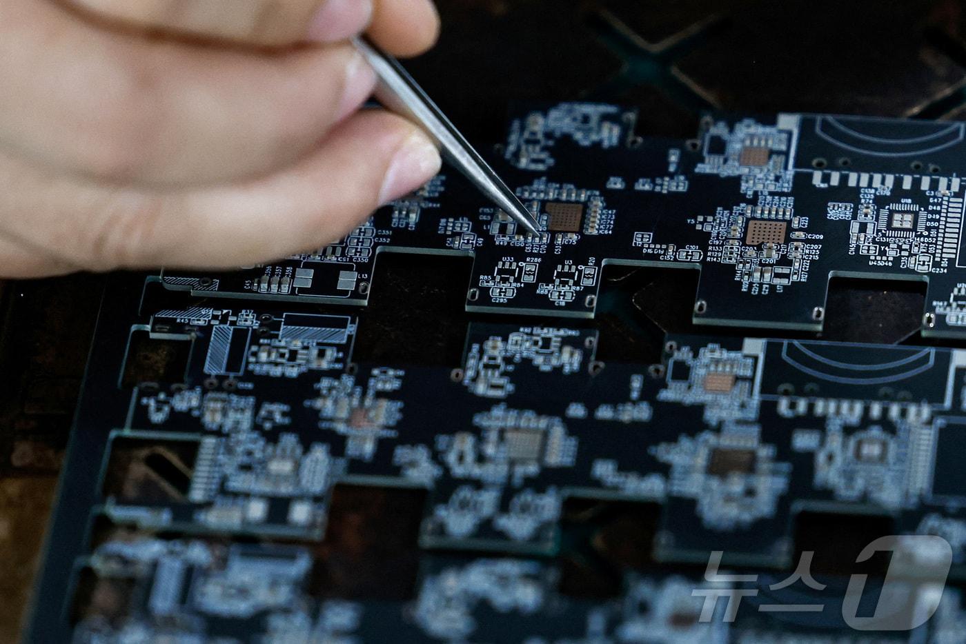 본문 이미지 - 중국 둥관의 한 공장에서 직원이 인쇄회로기판(PCB) 위에 마이크로칩과 전자 부품을 조정하고 있다. ⓒ 로이터=뉴스1