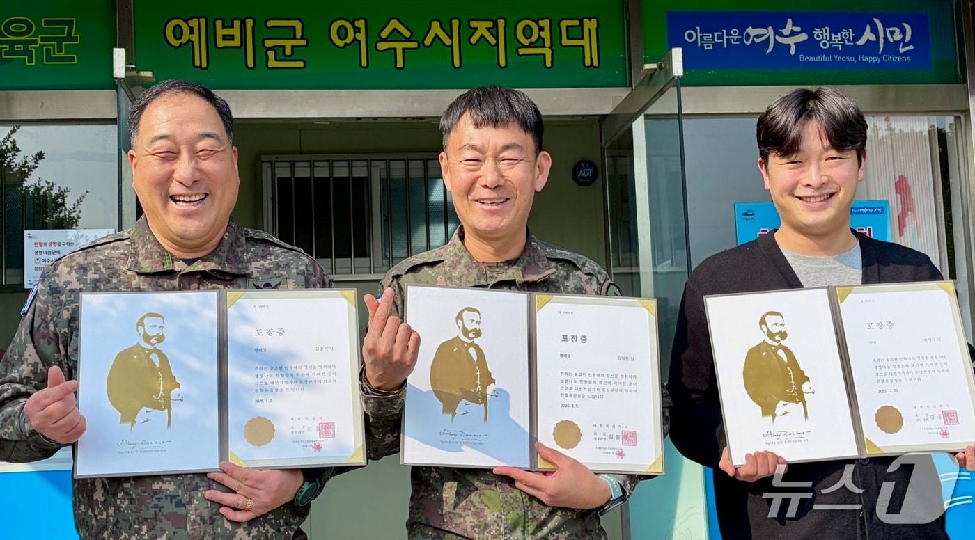 본문 이미지 - 육군 제31보병사단 여수시 예비군지역대 지휘요원들(왼쪽부터 김종국 여서동대장, 김정준 지역대장, 한상규 정작과장)이 지역대 앞에서 헌혈 유공 포장증을 들고 환하게 웃고 있다.(사진=31사단 제공. 재판매 및 DB 금지) 2026.4.3