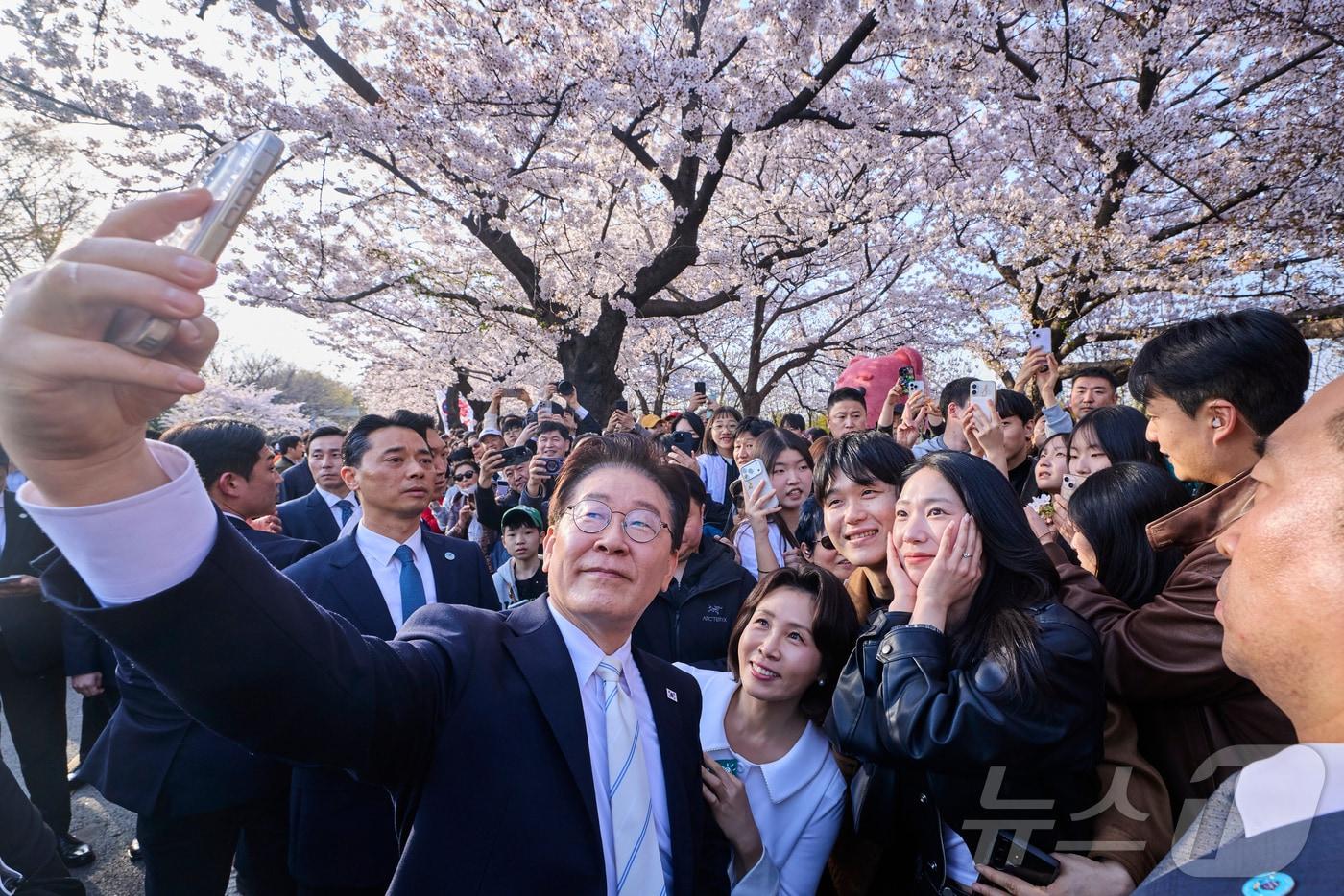 본문 이미지 - 이재명 대통령과 김혜경 여사가 5일 서울 여의도 윤중로를 찾아 벚꽃놀이 나온 시민들과 기념촬영을 하고 있다. (청와대 제공. 재판매 및 DB 금지) 2026.4.5 ⓒ 뉴스1 허경 기자