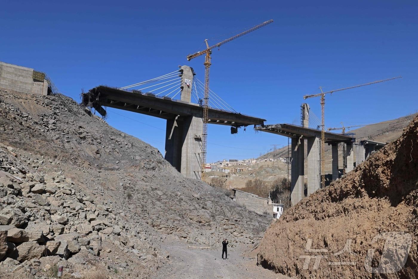 본문 이미지 - 3일(현지시간) 이란 카라즈에서 한 남성이 미국의 공습으로 파괴된 B1 교량을 촬영하고 있다. 튀르키예 아나돌루 통신에 따르면 이란 반(半)관영 파르스통신은 도널드 트럼프 미국 대통령이 B1 교량 파괴 영상을 공개한 직후인 2일 "역내 국가들의 주요 교량 여러 곳이 표적이 될 수 있다＂며 목록을 공개했다. 2026.04.03. ⓒ AFP=뉴스1