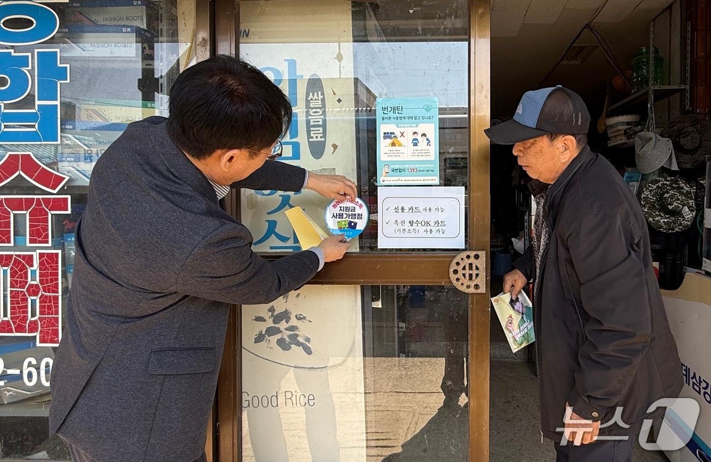본문 이미지 - 옥천군 직원이 시골마을 한 만물상을 찾아 농어촌 기본소득 사용처 매장을 스티커를 부착하고 있다.  (옥천군 제공. 재판매 및 DB금지)