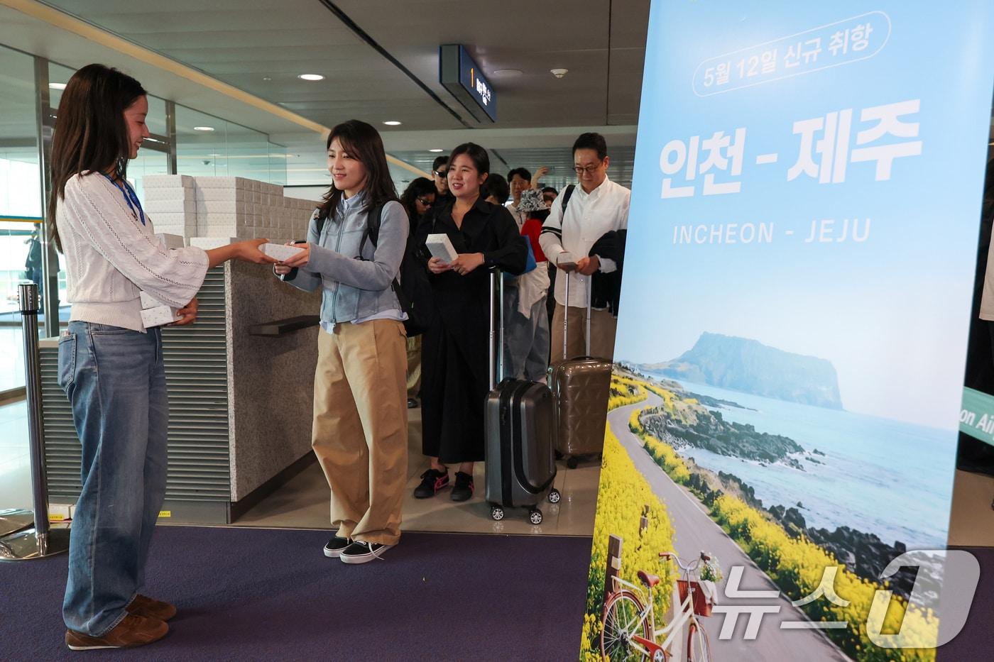 본문 이미지 - 인천-제주 국내선 직항노선이 10년만에 운영을 재개한 12일 인천국제공항 1터미널에서 제주로 향하는 제주항공 승객들이 기념품을 받고 있다. 2026.5.12 ⓒ 뉴스1 안은나 기자
