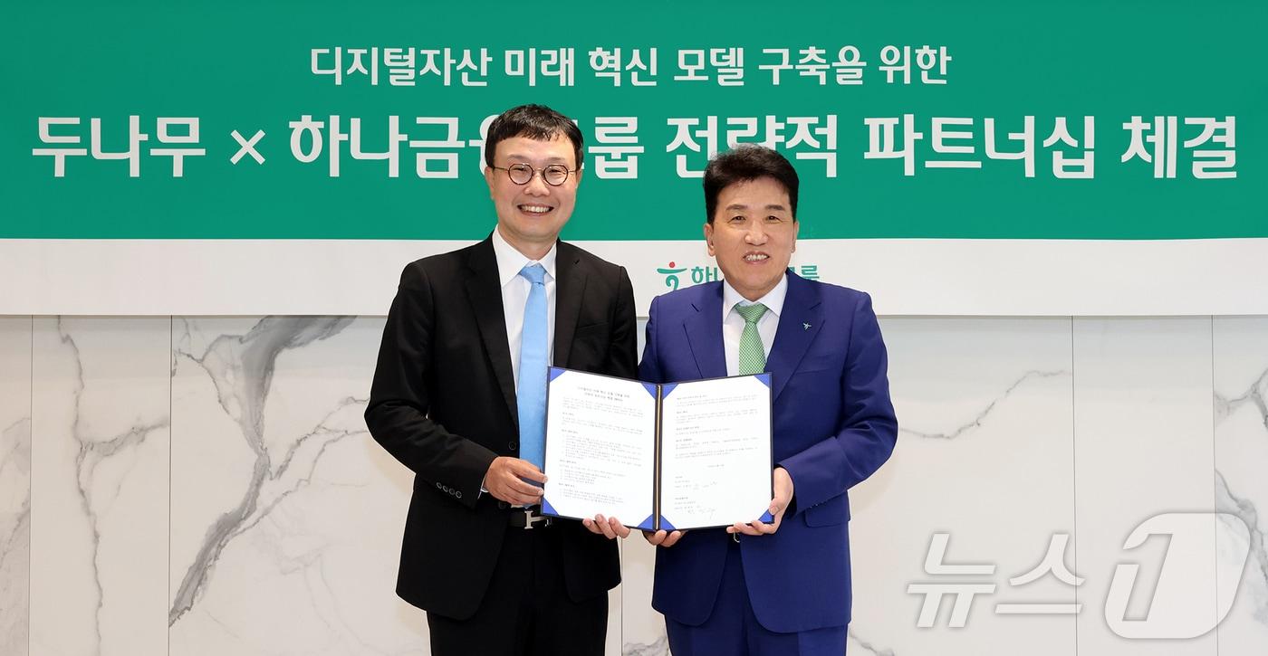 본문 이미지 - 하나금융그룹이 주요 관계사인 하나은행을 통해 국내 최대 가상자산 인프라를 보유한 두나무에 대한 1조원 규모 지분을 취득하고, 금융과 디지털자산을 연계한 미래혁신모델 구축을 위한 전략적 업무협약을 체결했다고 15일 밝혔다. 이날 협약식에 참석한 함영주 하나금융그룹 회장(오른쪽)이 김형년 두나무 부회장과 함께 협약서를 들고 기념촬영을 하고 있다. (하나은행 제공. 재판매 및 DB금지) 2026.5.15 ⓒ 뉴스1