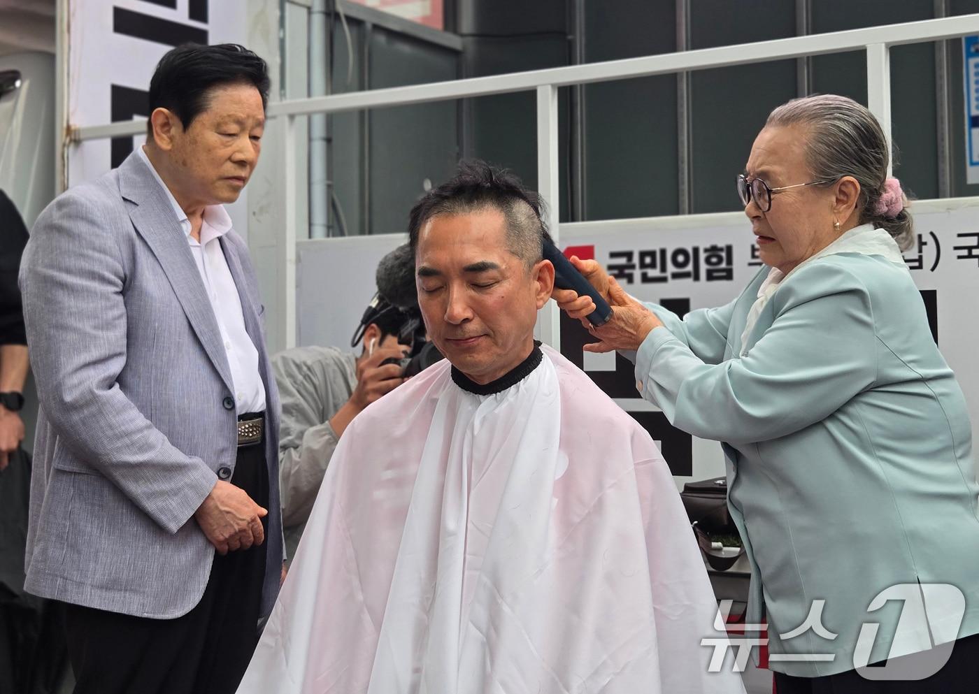 본문 이미지 -  6·3 지방선거 및 국회의원 재보궐선거 공식 선거운동 첫날인 21일 오후 부산 북구 구포시장 인근 쌈지공원에서 열린 국민의힘 박민식 후보 출정식에서 박 후보 모친이 아들의 삭발을 돕고 있는 모습. 2026.5.21 ⓒ 뉴스1 손승환