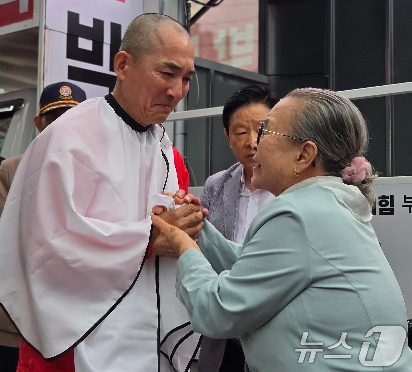 본문 이미지 - 박민식 국민의힘 부산 북구갑 국회의원 후보가 6·3 지방선거 및 국회의원 재보궐선거 공식 선거운동 첫날인 21일 오후 부산 북구 구포시장 인근 쌈지공원에서 열린 출정식에서 삭발한 뒤 박 후보 어머니의 손을 잡고 있다. 2026.5.21 ⓒ 뉴스1 손승환 기자
