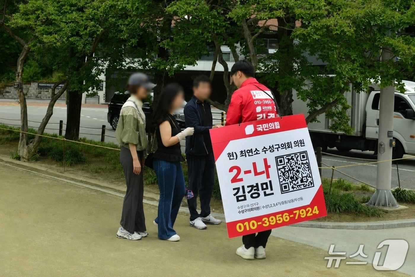 본문 이미지 - 22일 오전 대구 수성구 수성못에서 김경민 국민의힘 수성구의원(마선거구) 후보가 QR코드와 자신의 휴대전화 번호가 담긴 홍보물을 착용한 채 시민들에게 인사하며 선거운동을 하고 있다.2026.5.22 ⓒ 뉴스1 이성덕 기자
