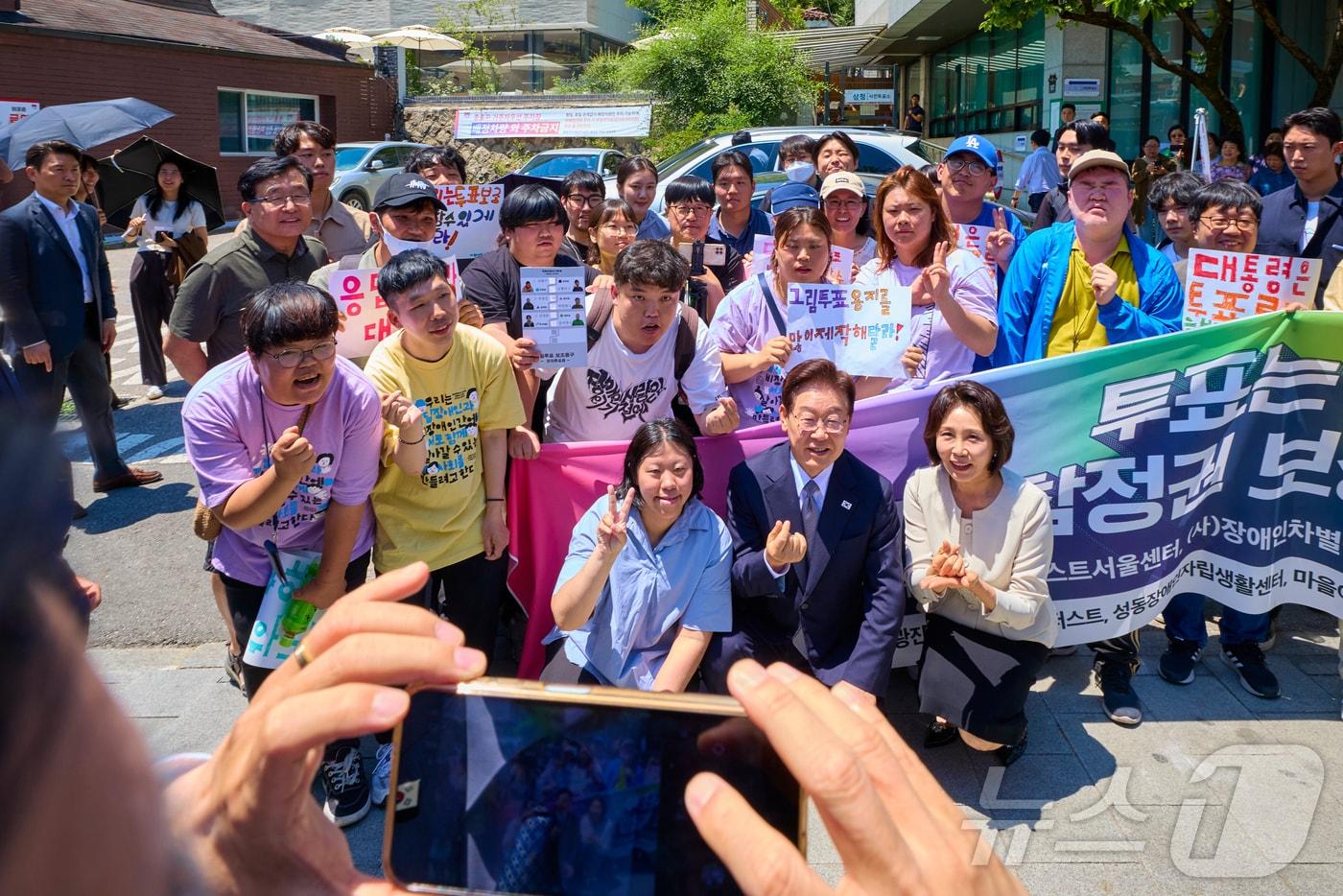 본문 이미지 - 이재명 대통령과 김혜경 여사가 29일 제9회 전국동시지방선거 사전투표를 하기 위해 서울 종로구 삼청동 주민센터에 마련된 투표소로 향하며 발달장애인 투표 참정권 보장을 촉구하는 시민단체와 기념촬영을 하고 있다. (청와대 제공. 재판매 및 DB 금지) 2026.5.29 ⓒ 뉴스1 허경 기자