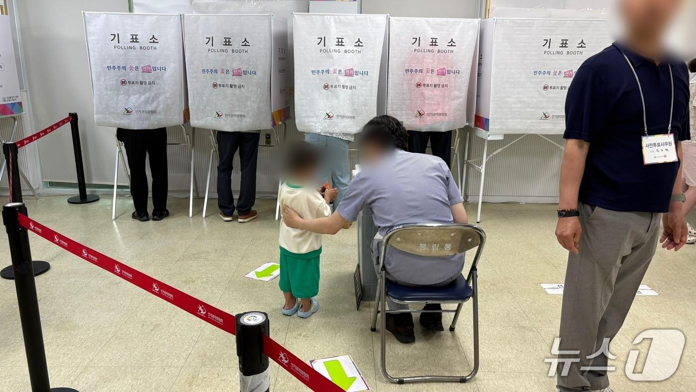 본문 이미지 - 6.3지방선거 사전투표 둘째 날인 30일 경남 창원시 봉림동 사전투표소에서 투표장 관계자가 기표소에 들어간 부모를 기다리는 아이를 잠시 돌봐주고 있다.2026.5.30/뉴스1 강정태 기자