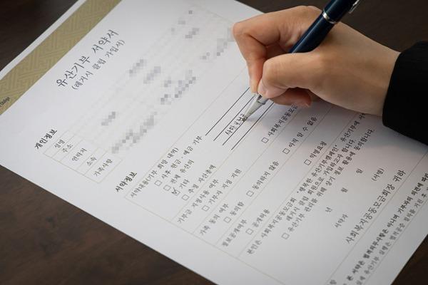 본문 이미지 - 사랑의열매 최연소 유산기부자인 A씨가 유산기부 서약서에 기부 자산으로 사망보험금을 기재하고 있다. (사랑의열매 제공)