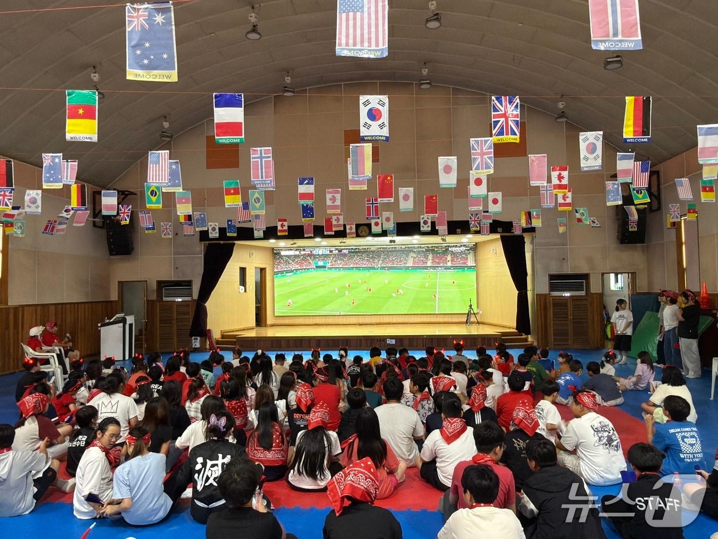 본문 이미지 - 우정초등학교 학생들이 강당에 설치된 대형 LED 전광판으로 2026 FIFA 월드컵 대한민국-체코전을 함께 관람하며 응원하고 있다. (우정초등학교 제공) 