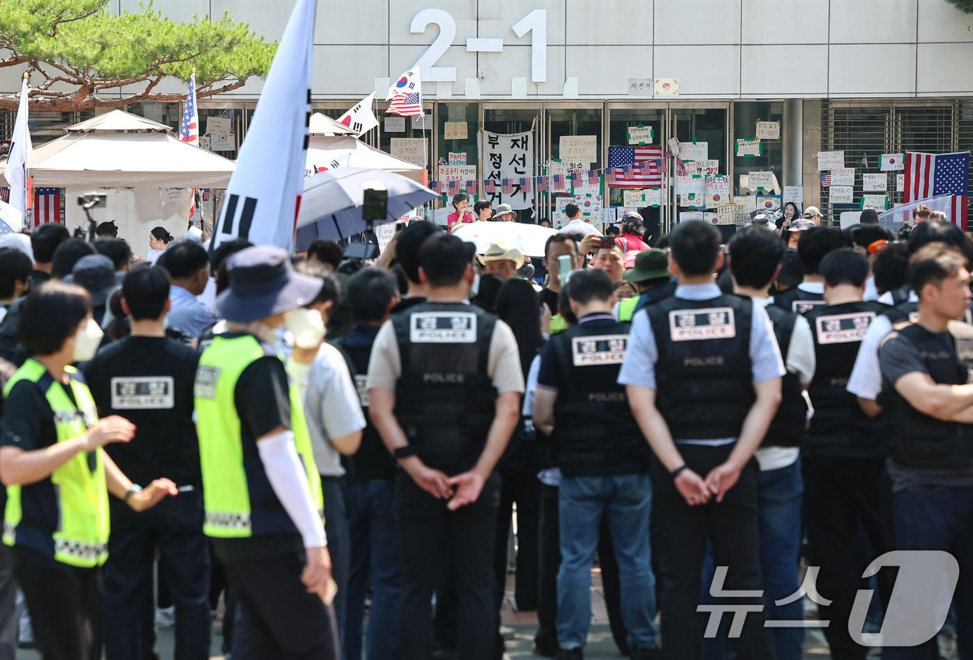 본문 이미지 - 6·3 지방선거 '투표용지 부족 사태'로 12일째 잠실 개표소 봉쇄 시위가 이어지고 있는 16일 경찰과 대한체육회 등관계자들이 서울 송파구 올림픽공원 핸드볼경기장 진입을 시도하다 시위대와 대치하고 있다. 2026.6.16 ⓒ 뉴스1 김도우 기자