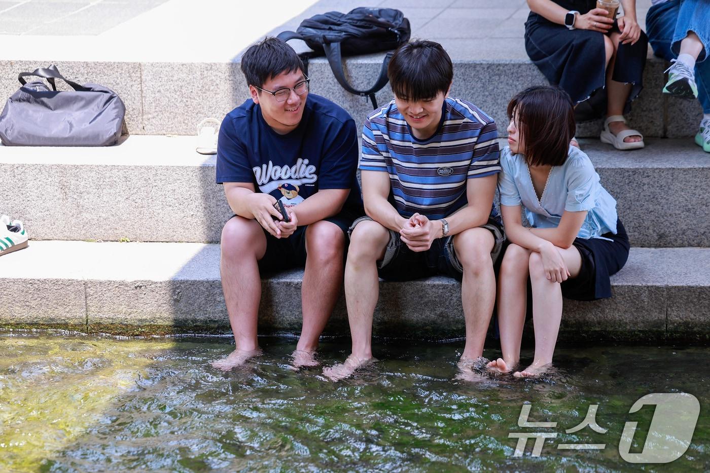 본문 이미지 - 서울 낮 최고기온 33도로 무더운 날씨가 이어진 16일 오후 서울 종로구 청계천을 찾은 시민들이 발을 담그며 대화하고 있다. 2026.6.16 ⓒ 뉴스1 안은나 기자