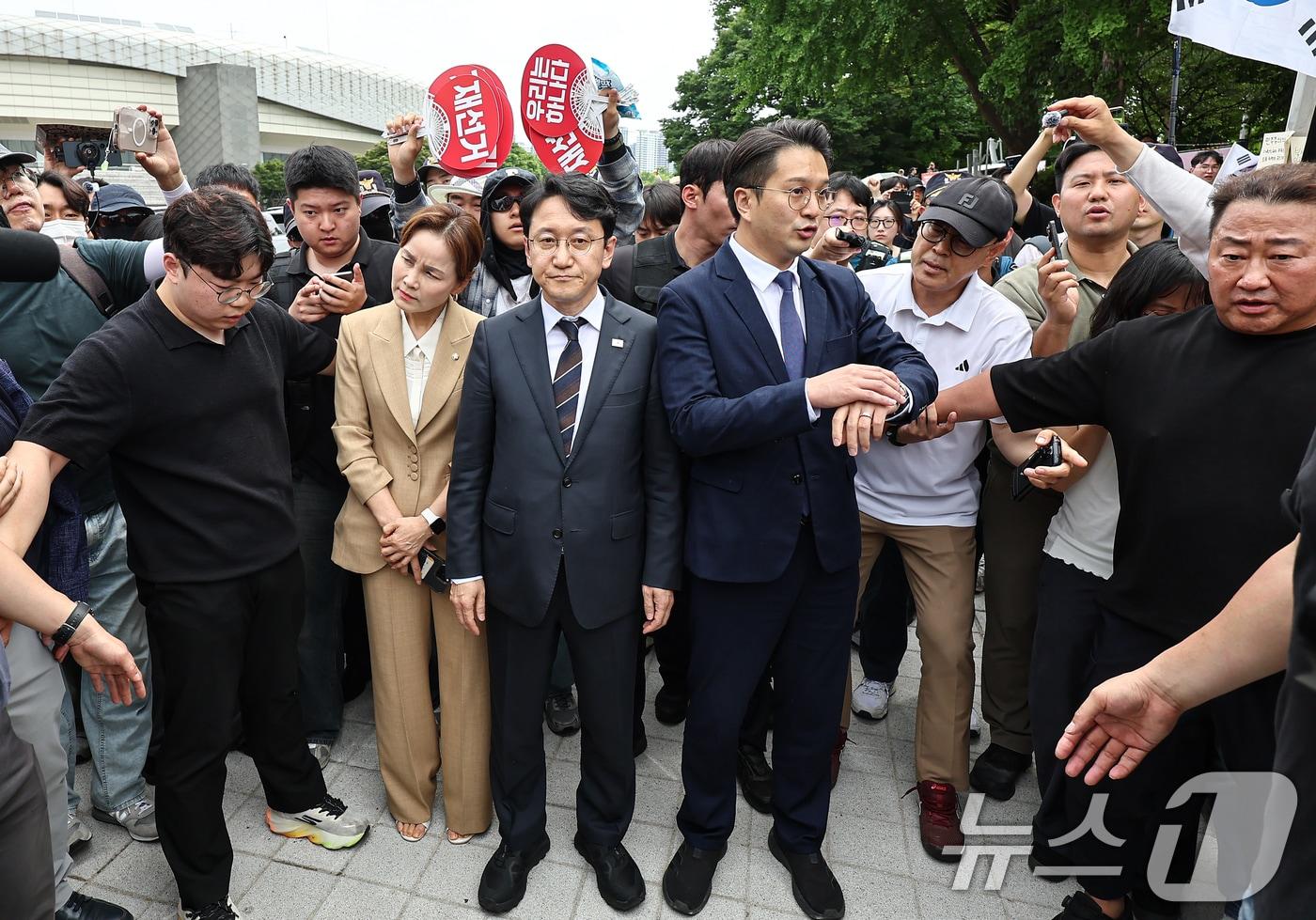 본문 이미지 - 임오경, 전용기, 천준호 더불어민주당 의원이 17일 서울 송파구 올림픽공원 핸드볼경기장 앞에서 투표용지 부족 사태를 규탄하는 시민들에게 항의를 받으며 이동하고 있다. 2026.6.17 ⓒ 뉴스1 김도우 기자