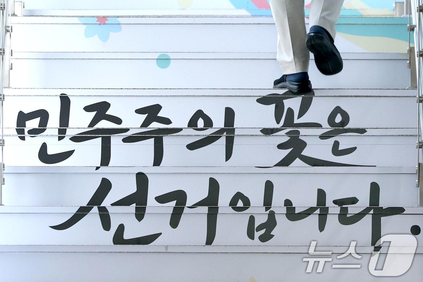 본문 이미지 - 6.3지방선거 투표용지 부족 사태를 수사하는 검경 합동수사본부가 본격 가동된 17일 경기도 과천 중앙선거관리위원회에서 '민주주의 꽃은 선거입니다'라고 적힌 계단을 한 직원이 올라가고 있다. 2026.6.17 ⓒ 뉴스1 이광호 기자