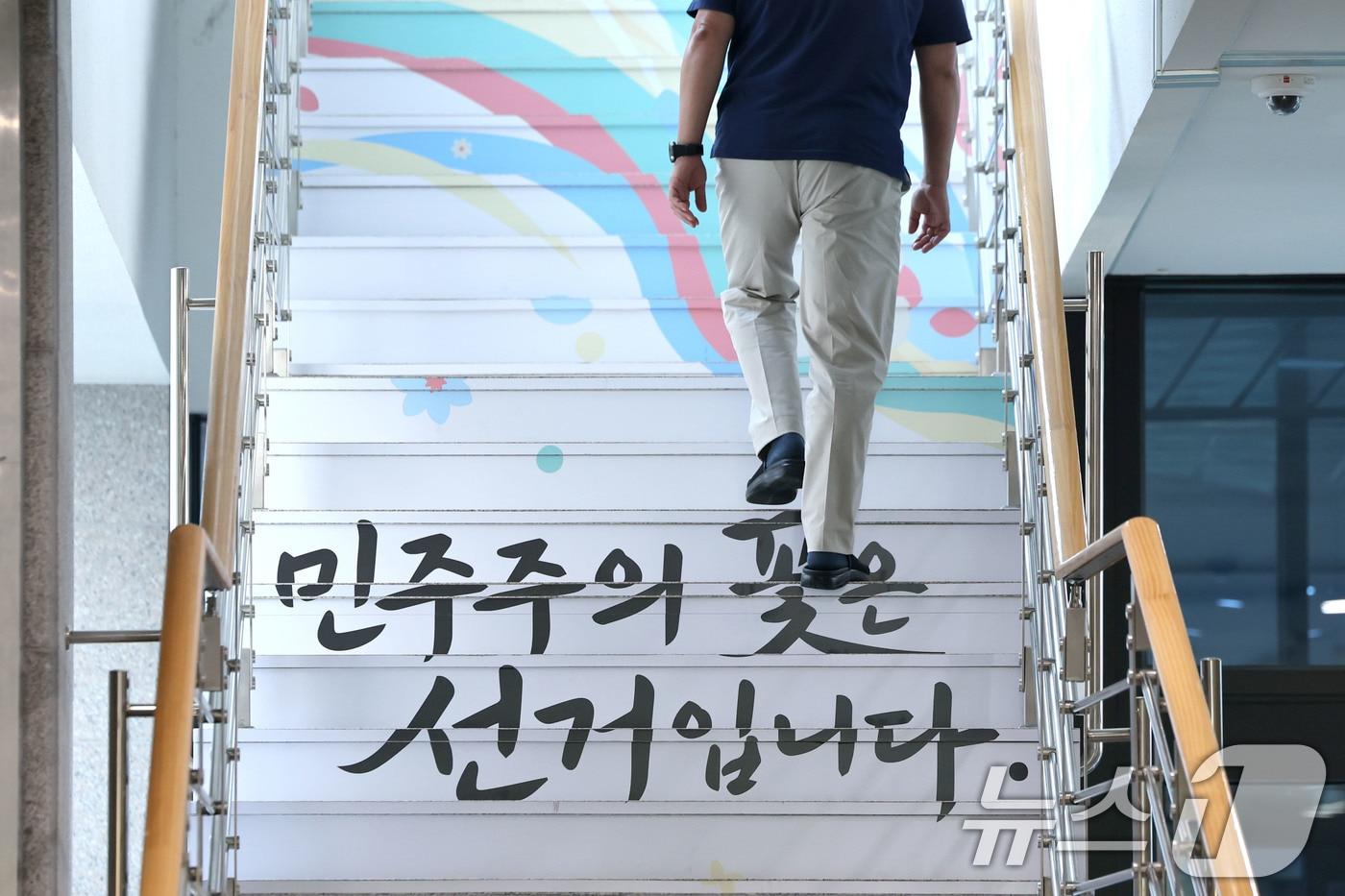 본문 이미지 - 6.3지방선거 투표용지 부족 사태를 수사하는 검경 합동수사본부가 본격 가동된 17일 경기도 과천 중앙선거관리위원회에서 '민주주의 꽃은 선거입니다'라고 적힌 계단을 한 직원이 올라가고 있다. 2026.6.17 ⓒ 뉴스1 이광호 기자