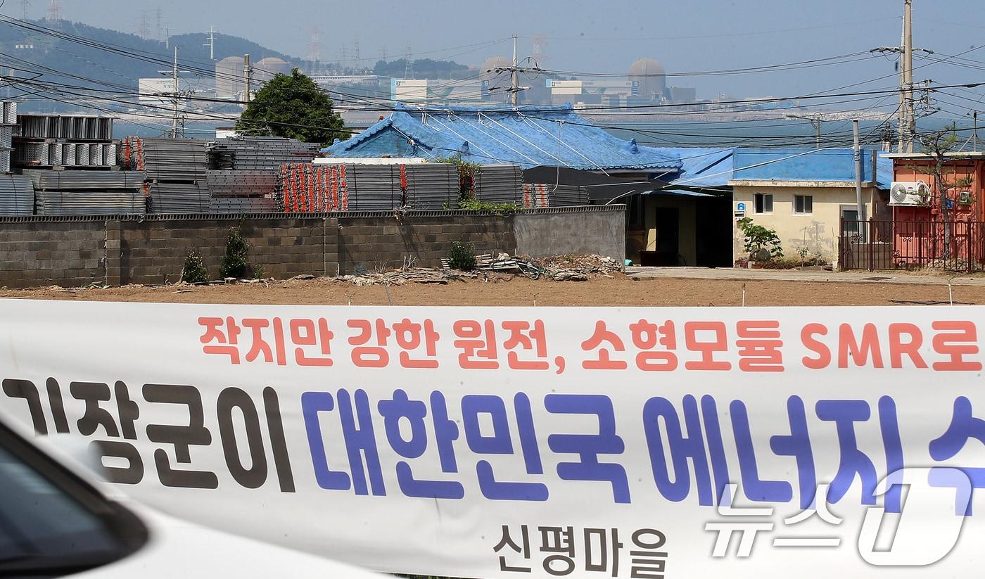본문 이미지 - 신규원전건설 부지선정평가위원회가 제11차 전력수급기본계획에 반영된 신규 원전 건설 후보부지로 대형원전은 경북 영덕군, 국내 첫 상용 소형모듈원전(SMR)은 기장군을 각각 선정한 가운데 18일 부산 기장군 신평마을회관 인근 도로변에 내걸린 SMR 기장군 유치를 바라는 내용의 현수막 뒤로 고리1, 2, 3, 4호기가 보이고 있다. 2026.6.18 ⓒ 뉴스1 윤일지 기자