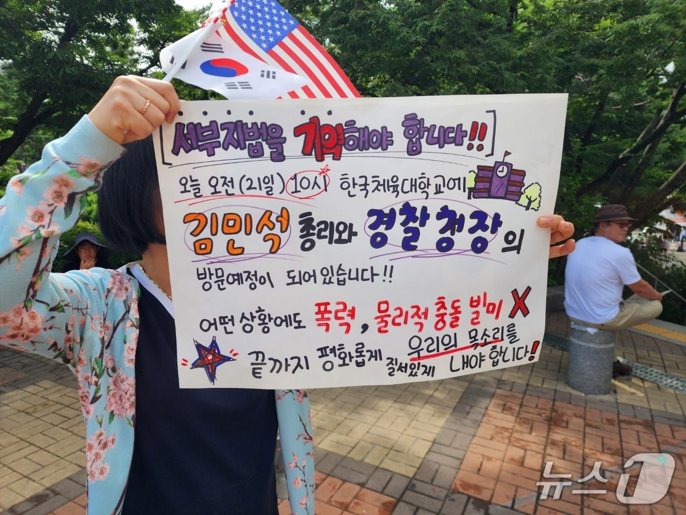 본문 이미지 - 21일 서울시 송파구 올림픽공원 핸드볼경기장 인근에서 비폭력 시위를 주장하는 여성이 피켓을 들고 홍보하고 있다. 2026.06.21/ⓒ 뉴스1 권진영 기자